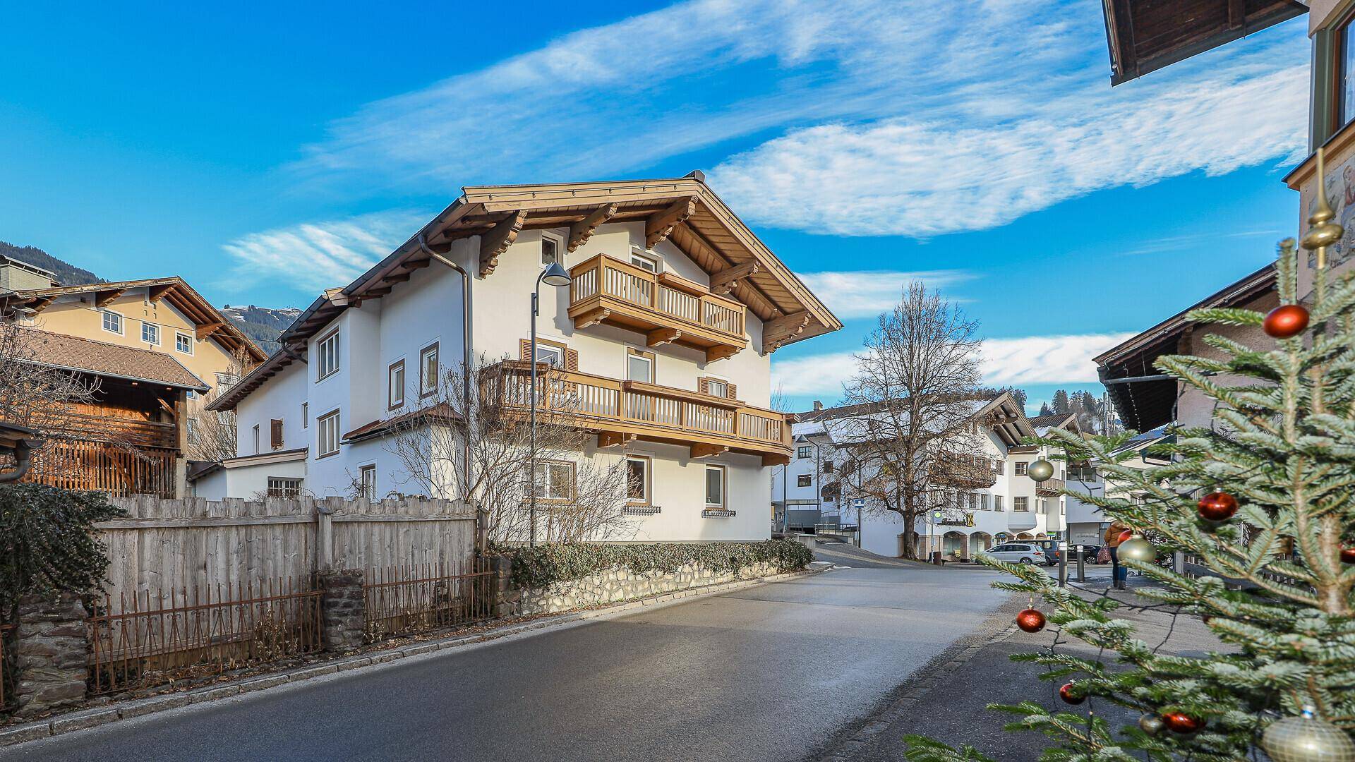 Traditionelles Haus mit Holzbalkonen und Satteldach in winterlicher Berglandschaft, geschmückt mit einem Weihnachtsbaum.