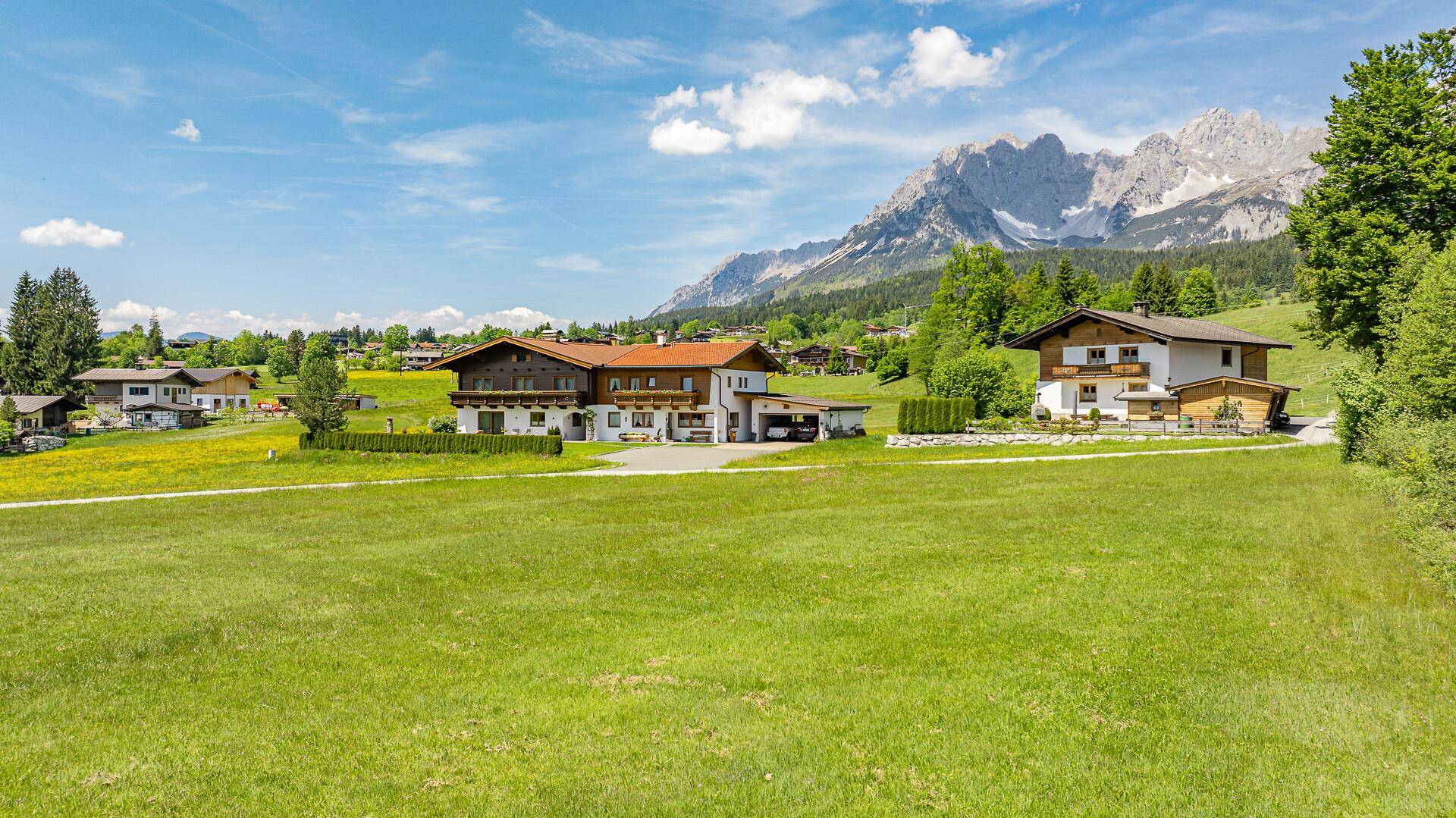 Traditionelle Häuser in einer weitläufigen grünen Landschaft mit majestätischen Bergen im Hintergrund.