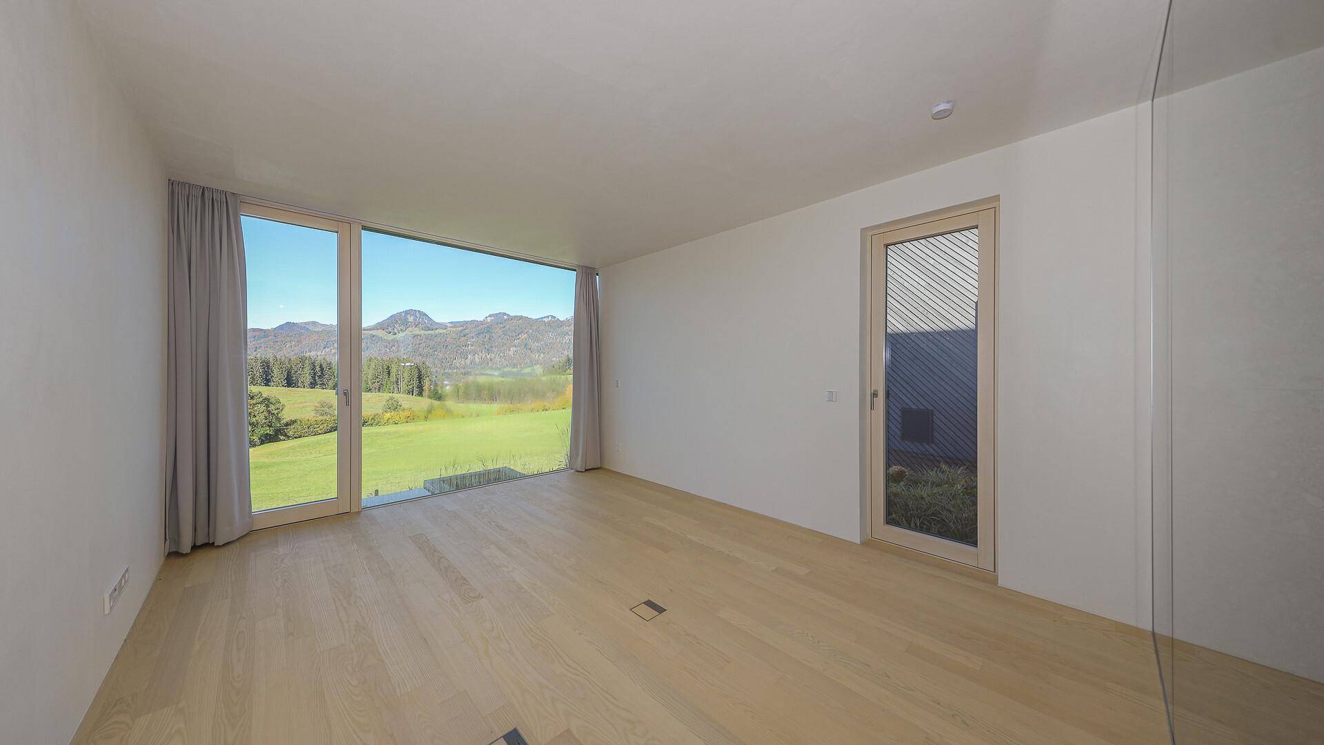 Geräumiges, unmöbliertes Schlafzimmer mit Holzboden und weitem Blick auf die Landschaft.