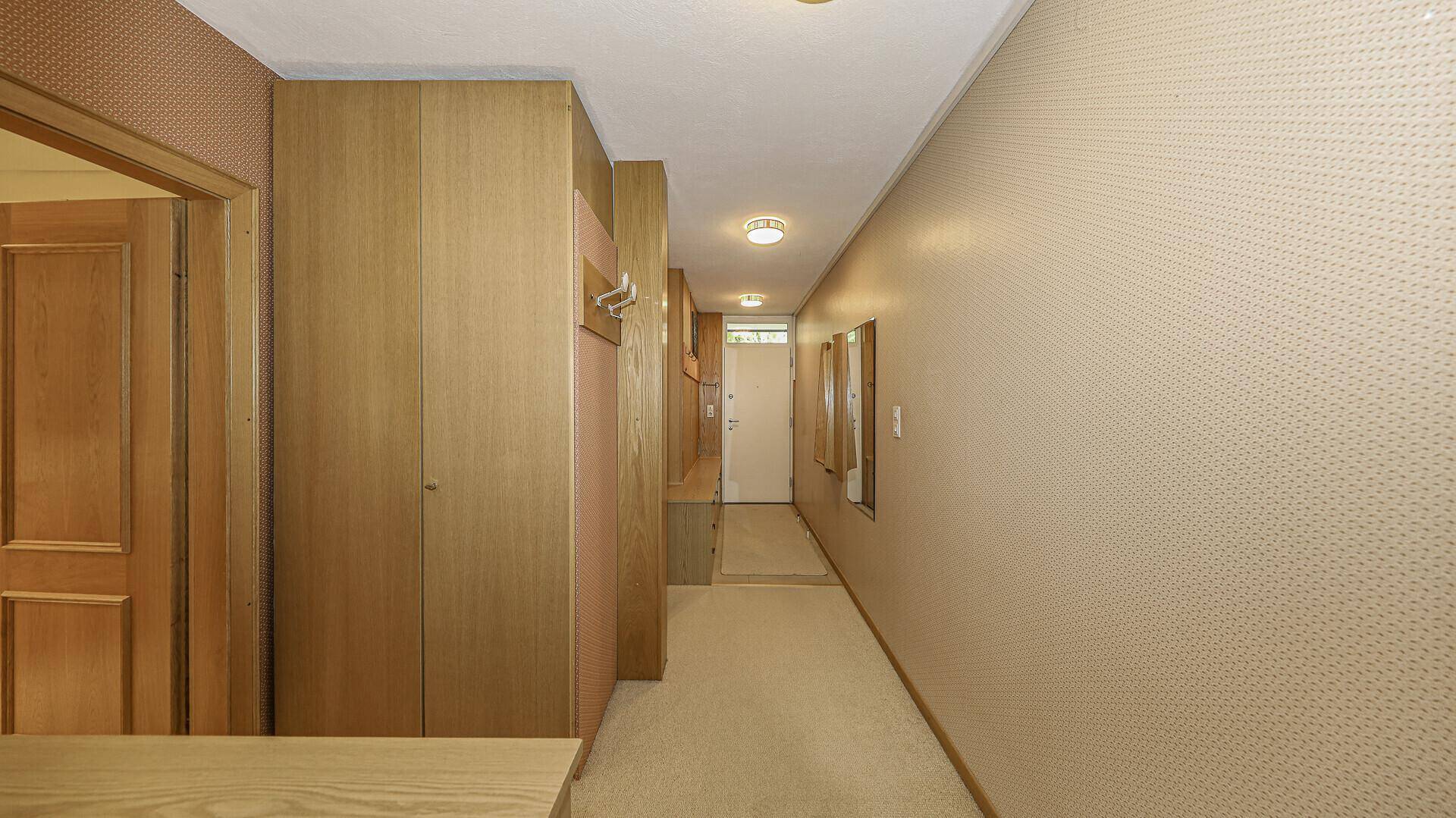 Langer Flur mit Holzverkleidung und Teppichboden, führt zu weiteren Räumen.