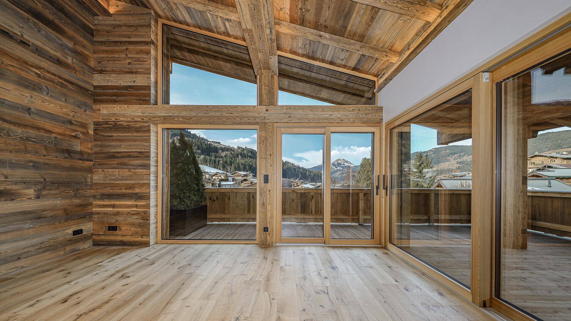 Helles Wohnzimmer mit viel Holz, hohen Decken und Zugang zu einer Terrasse mit Bergblick.