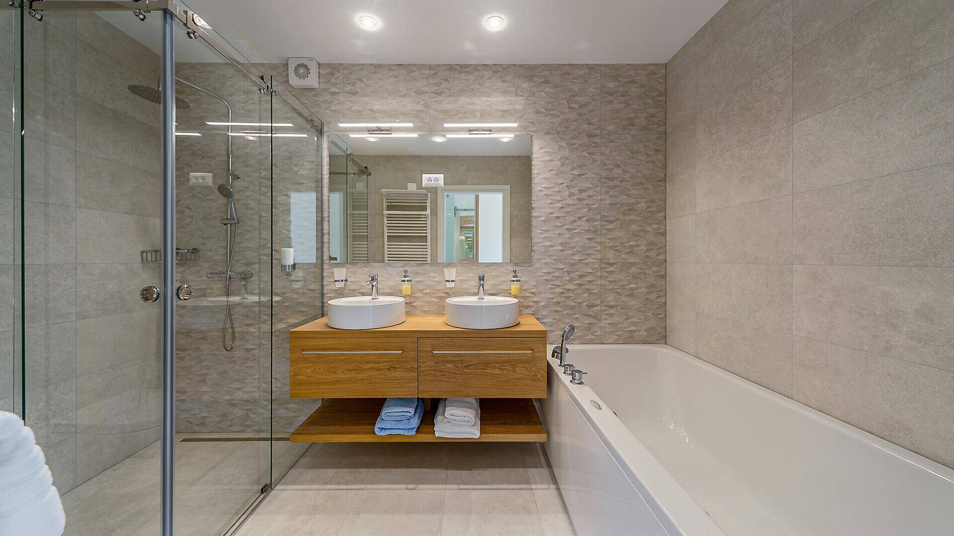 Stilvolles Badezimmer mit begehbarer Dusche, Badewanne und Doppelwaschbecken auf einem Holzunterschrank.
