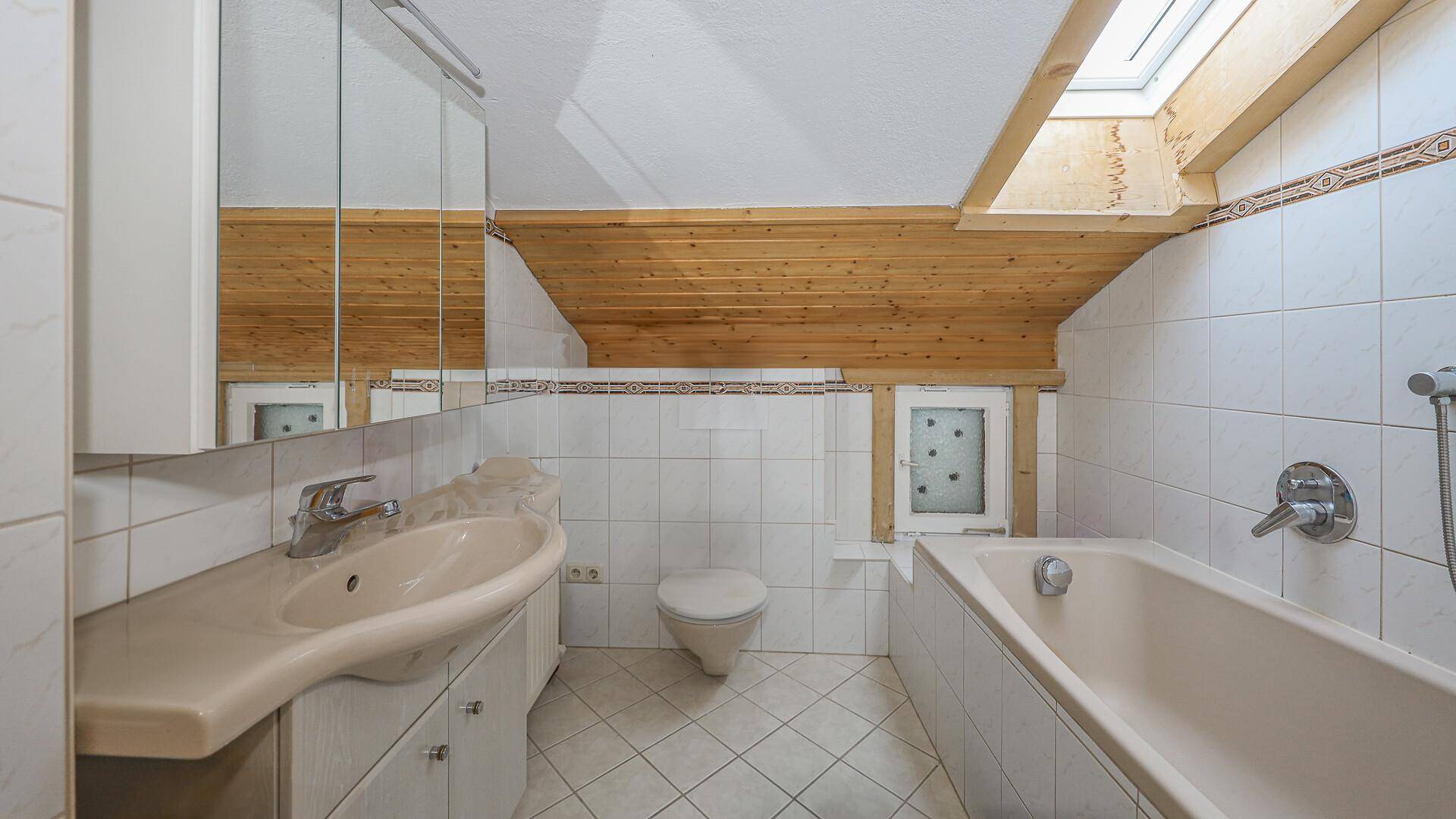 Badezimmer im Dachgeschoss mit Badewanne, Waschbecken und Dachfenster, hell gefliest.