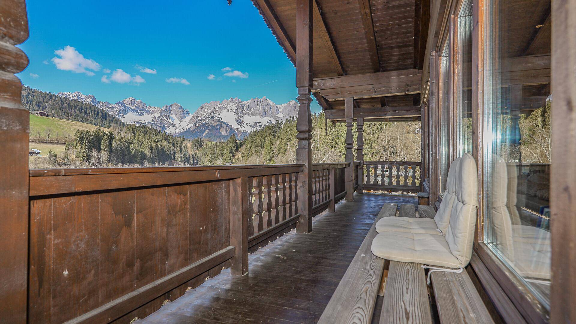 Langer Holzbalkon mit Sitzgelegenheiten und Panoramablick auf die umliegende Berglandschaft.