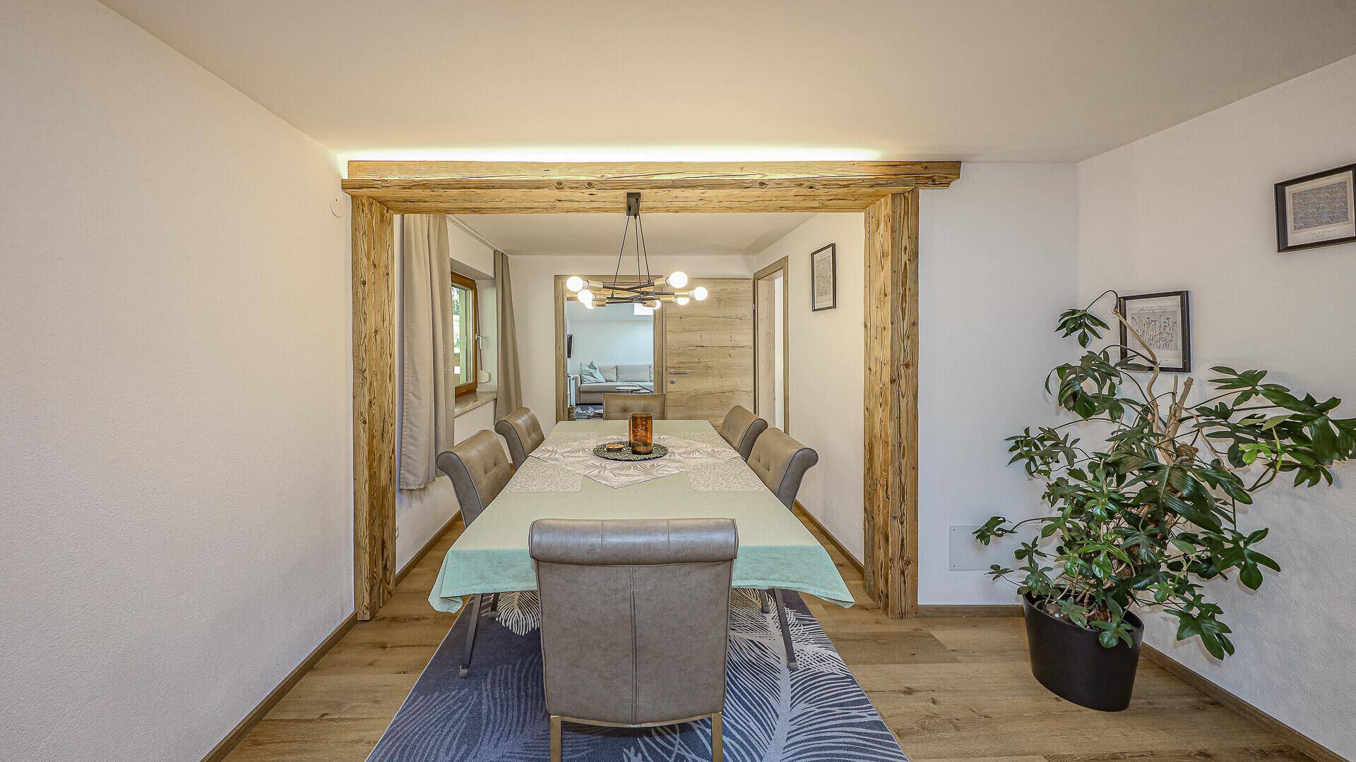 Gemütlicher Essbereich mit großem Holztisch, bequemen Stühlen und rustikalen Holzbalken als Raumteiler.