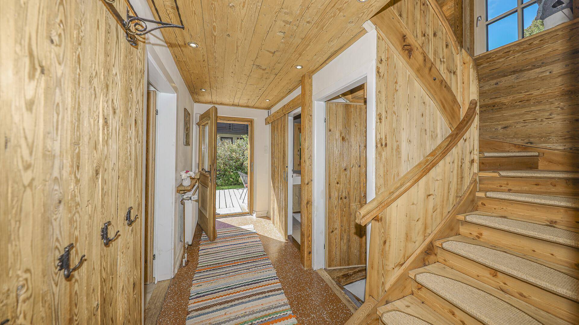 Heller Flur mit Holzvertäfelung, Holztreppe und Zugang zu den Zimmern.