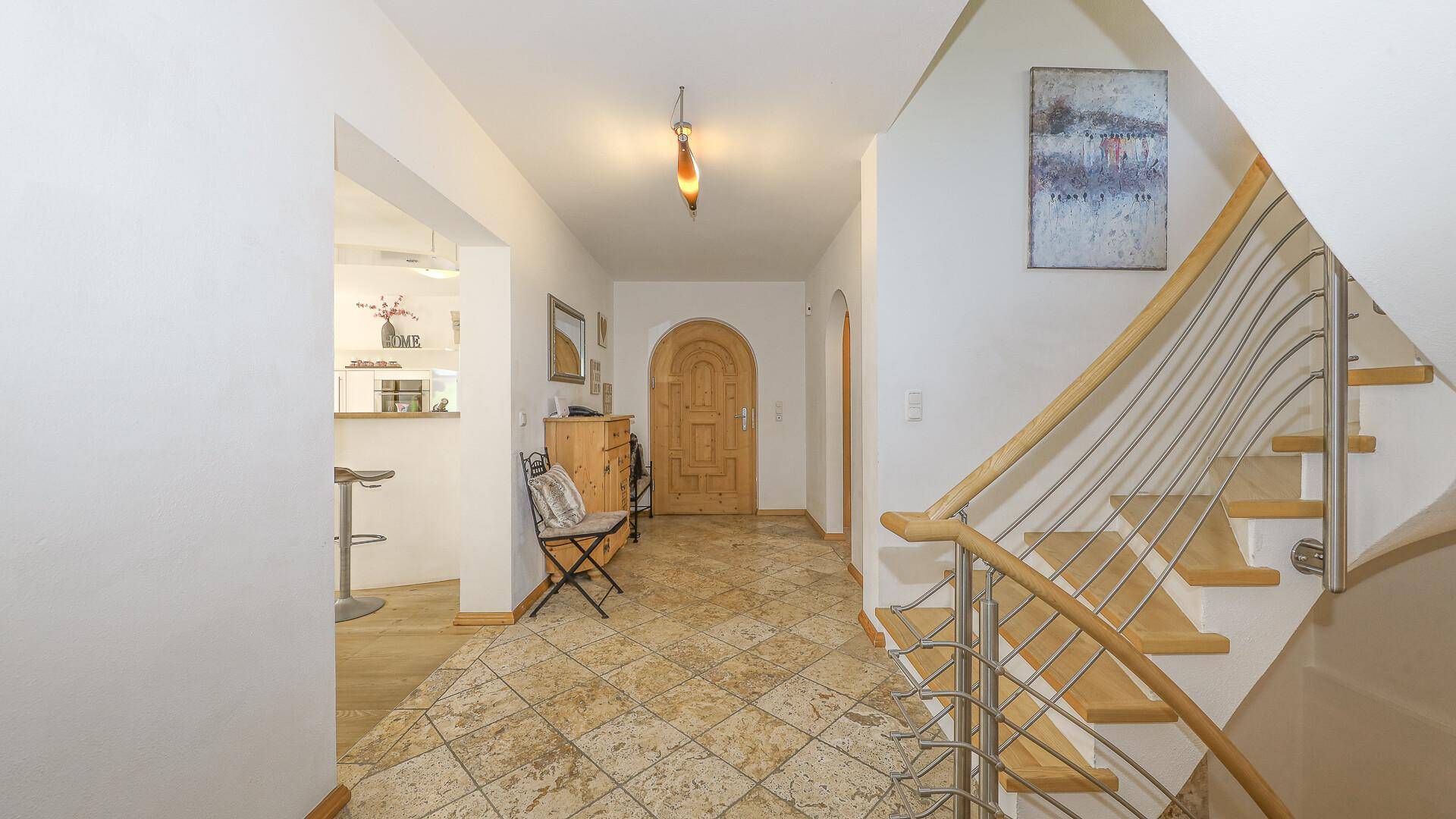 Heller Flur mit Steinfliesenboden und eleganter Treppe, die in die oberen Stockwerke führt.