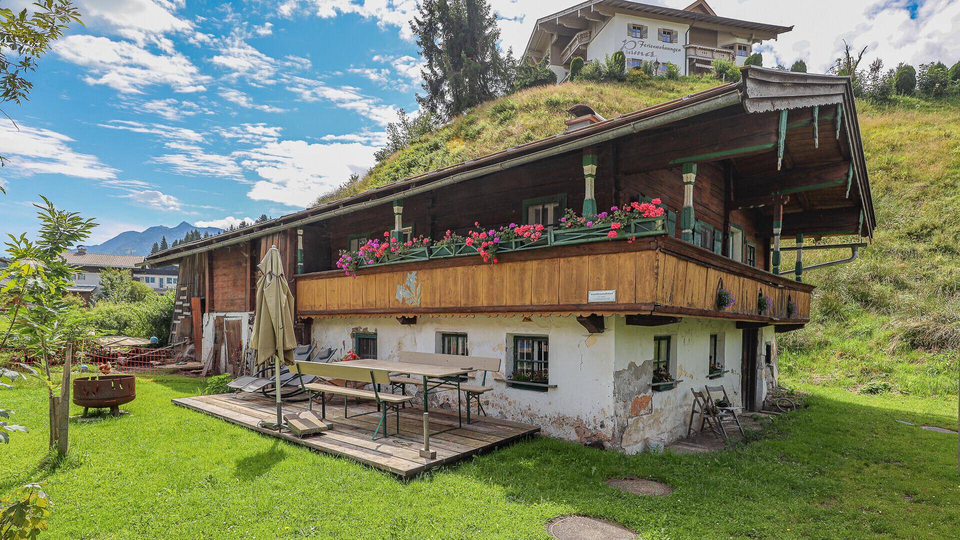 Rustikales Holzhaus mit Terrasse und Balkon, umgeben von grüner Hügellandschaft.