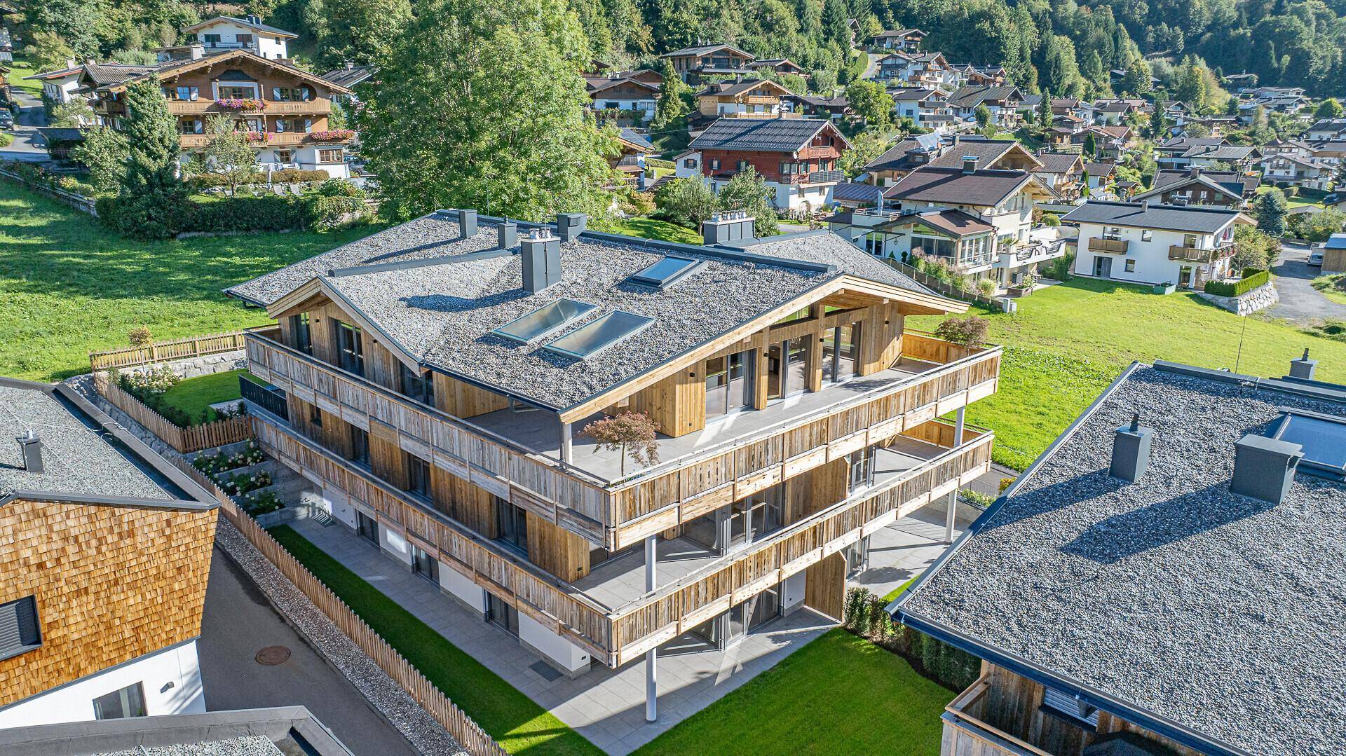 Luftaufnahme eines modernen Mehrfamilienhauses im alpinen Stil mit Satteldach und Dachfenstern.