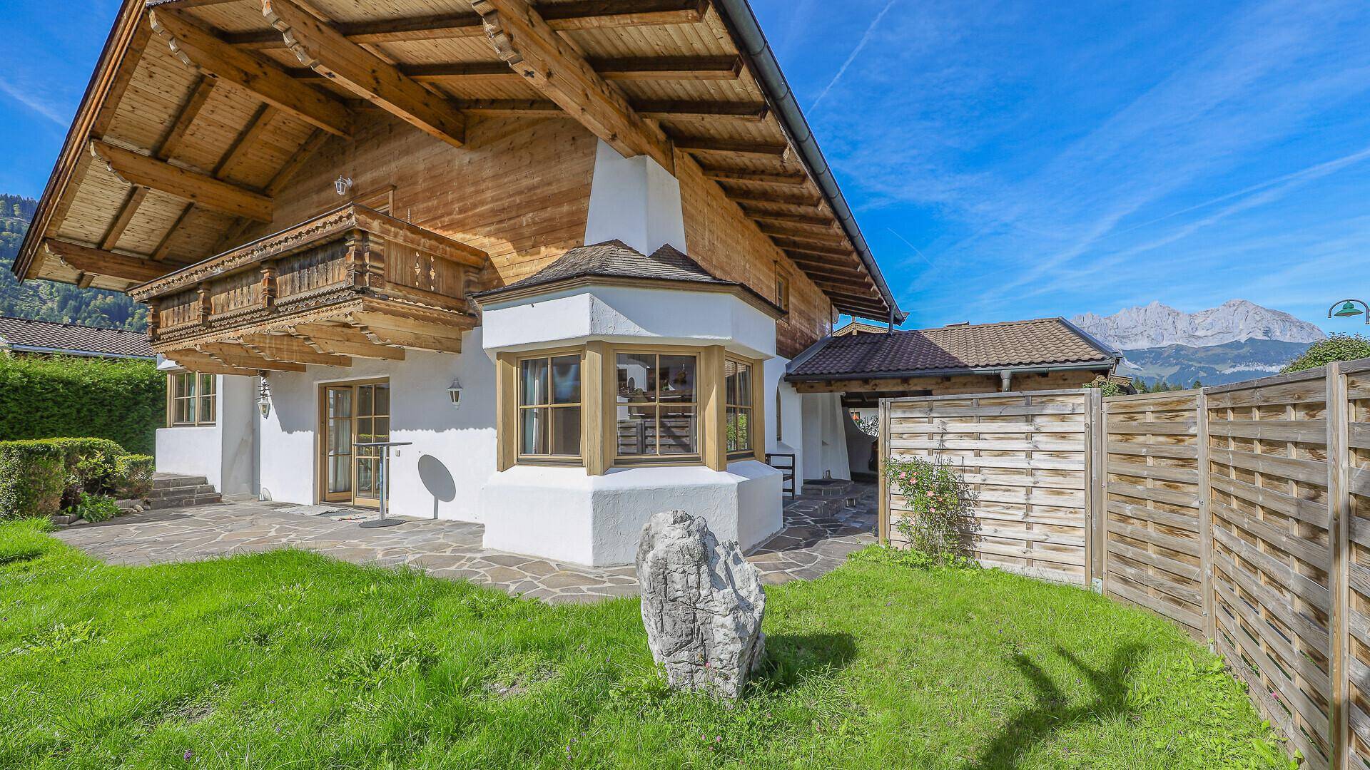 Rückseite des Chalets mit gepflastertem Bereich, Rasen und Bergblick.
