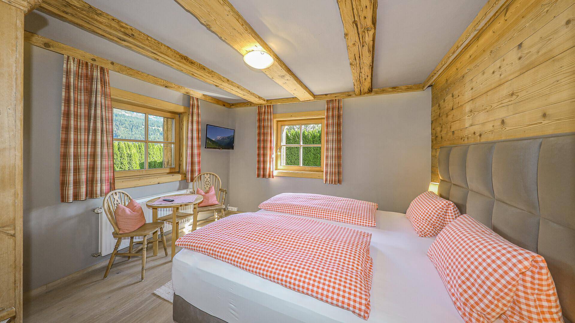 Gemütliches Schlafzimmer mit Doppelbett, Holzbalken und traditionellen Vorhängen.