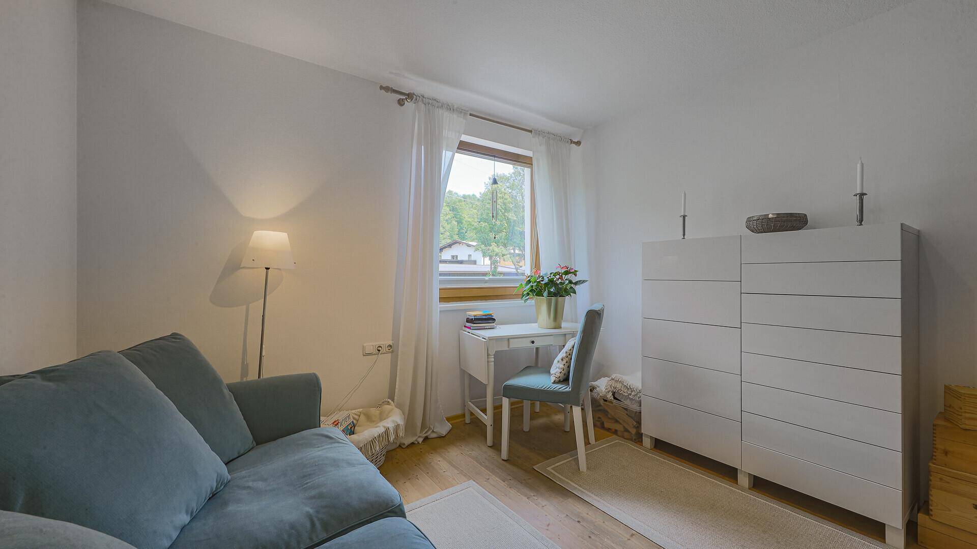 Gemütliches Zimmer mit blauem Sofa, Schreibtisch und viel Tageslicht.