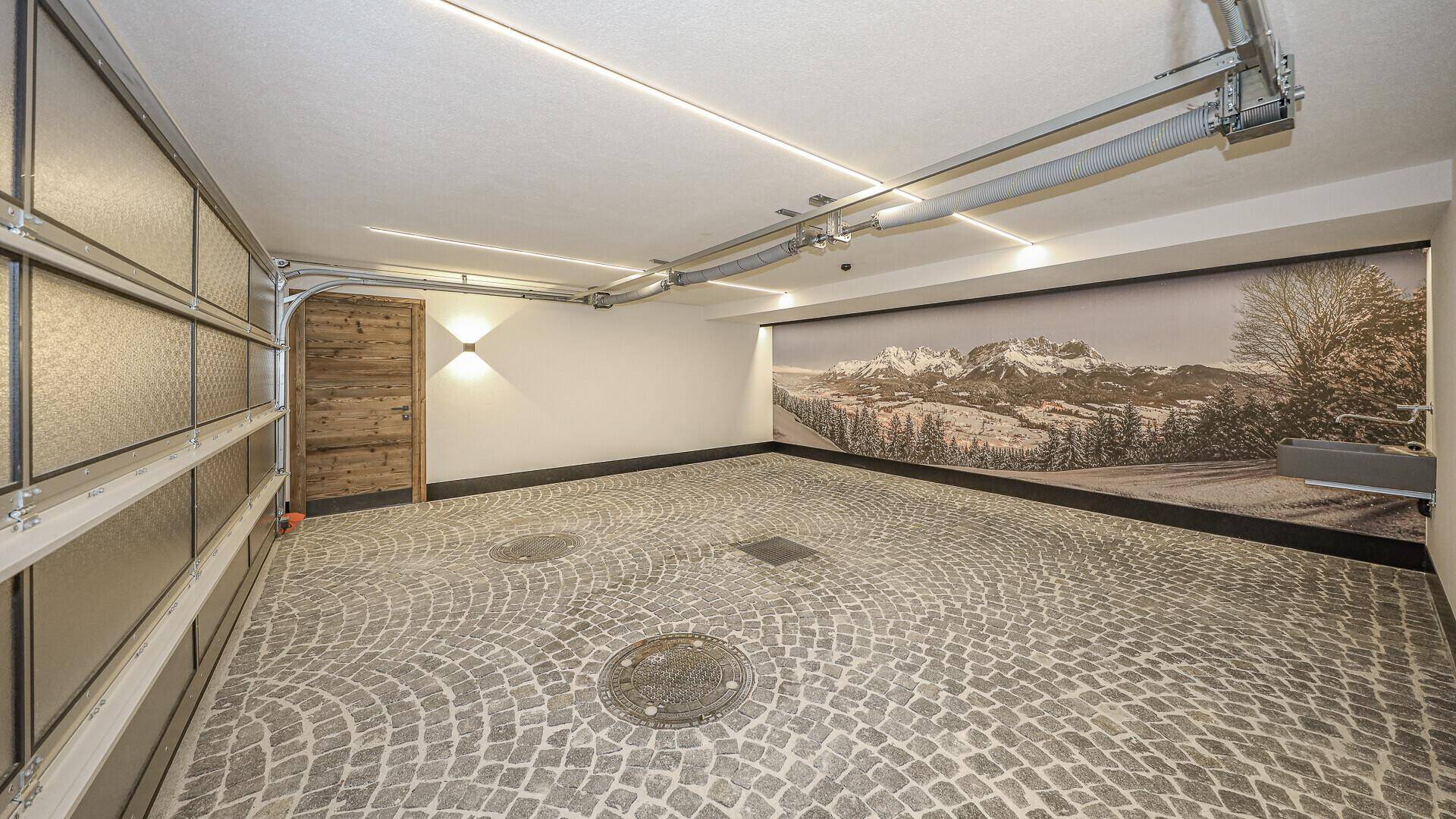 Geräumige Tiefgarage mit Kopfsteinpflasterboden und Wandbild einer Berglandschaft.