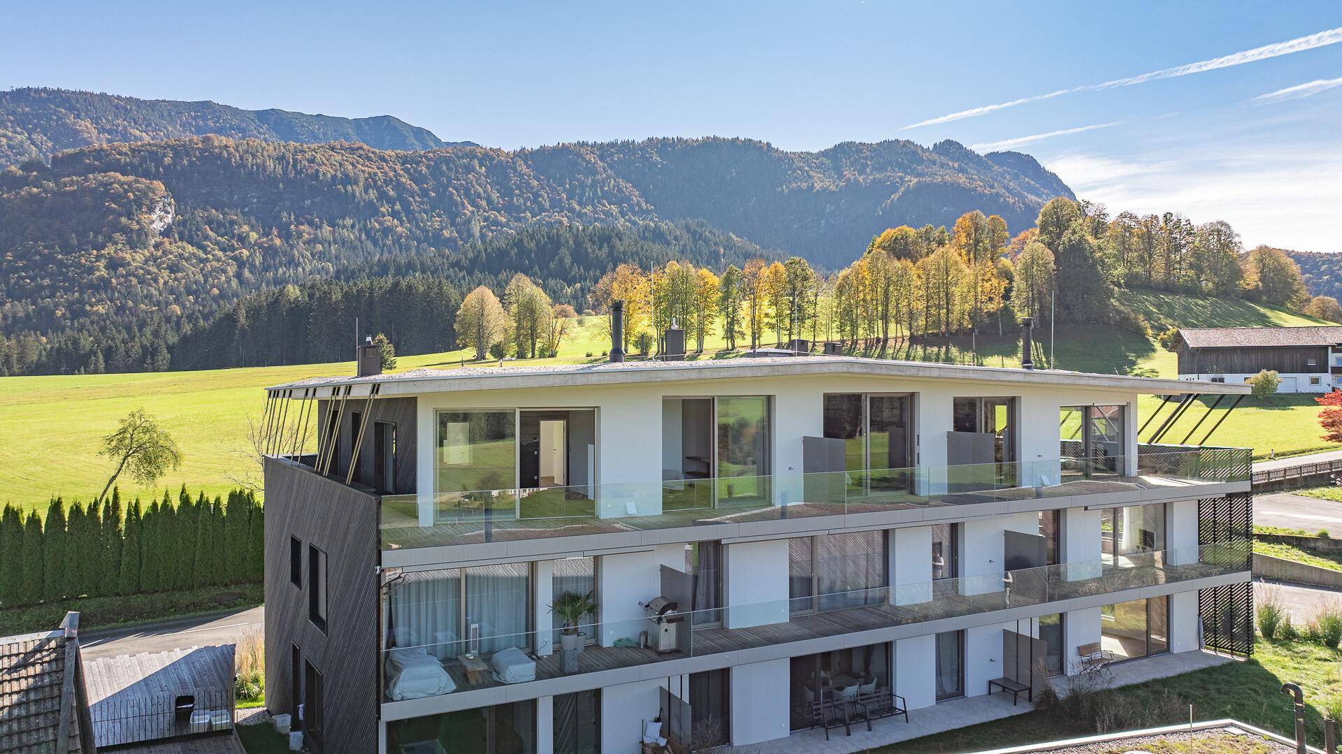 Moderne Wohnanlage mit großen Balkonen und Glasbrüstungen vor einer grünen Bergkulisse.