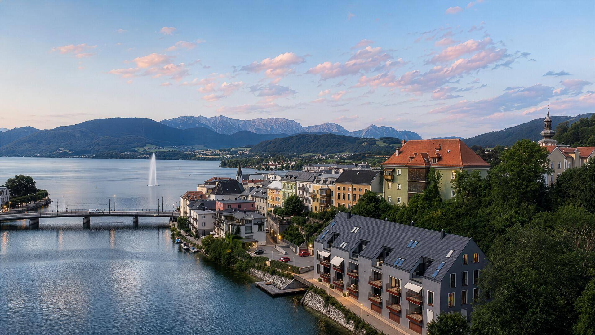 Panoramablick über die Stadt am See mit majestätischen Bergen im Hintergrund bei Sonnenuntergang.