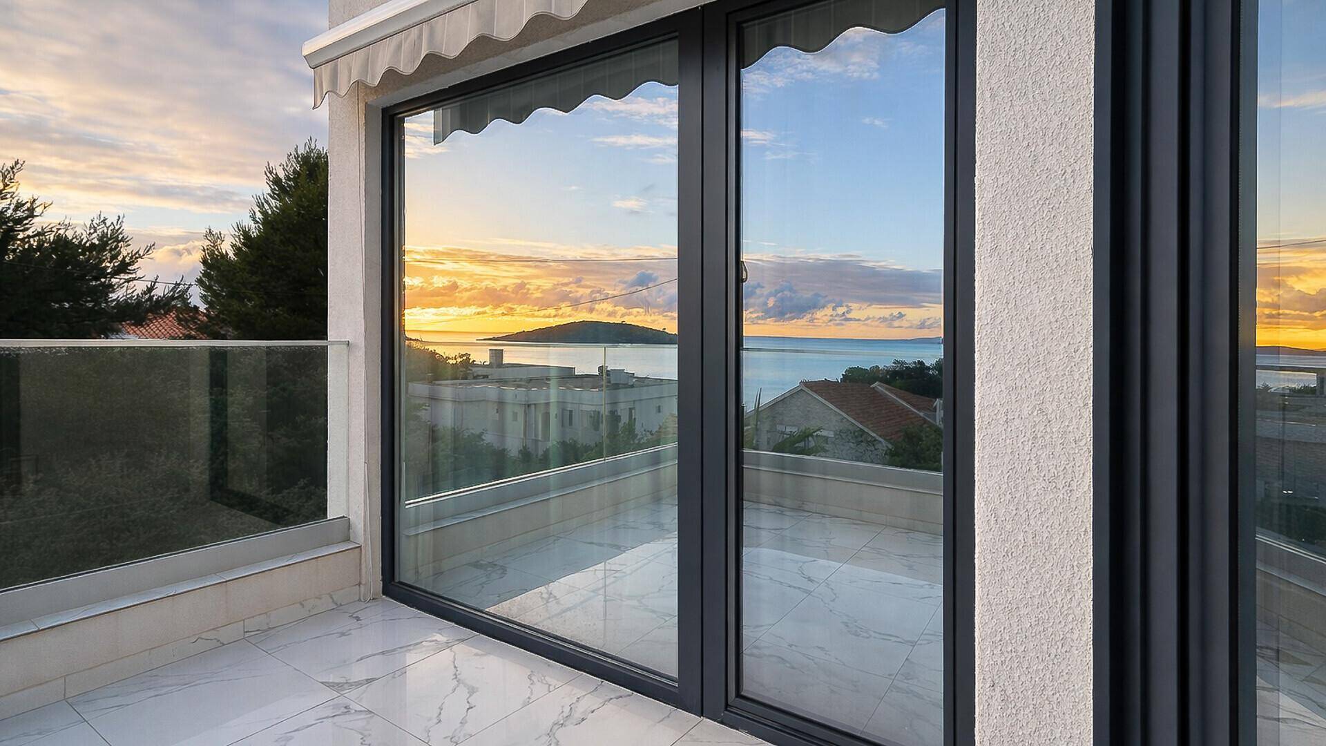 Balkon mit großen Glasfenstern und atemberaubendem Blick auf das Meer und den Sonnenuntergang.