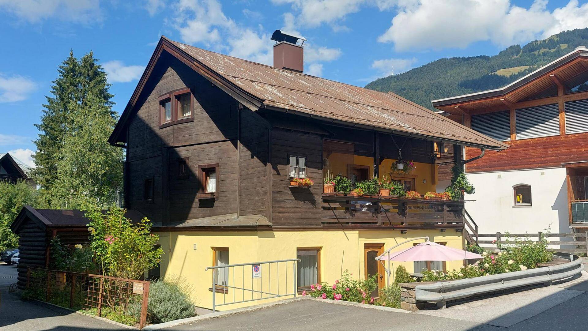 Traditionelles Holzhaus mit gelbem Sockel und einem blumengeschmückten Balkon.