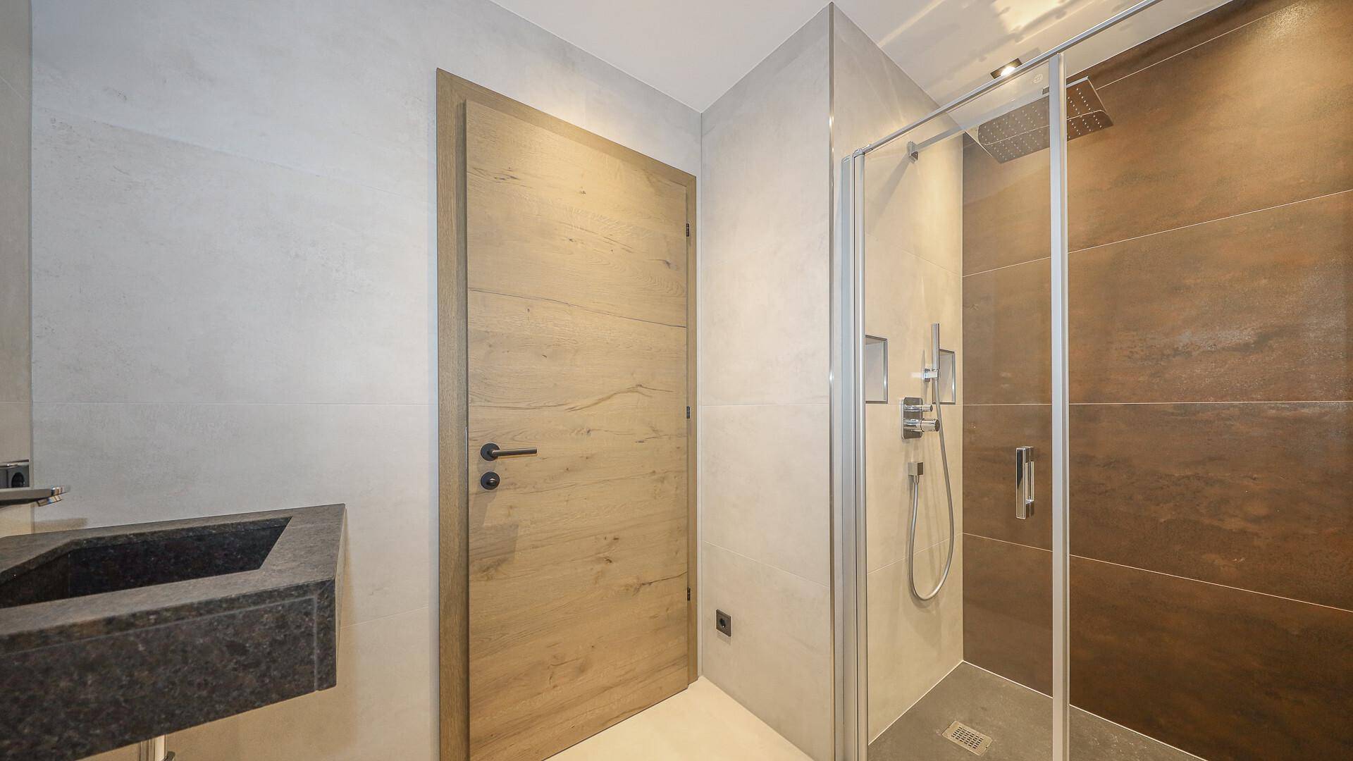 Modernes Badezimmer mit begehbarer Dusche, schwebendem Waschbecken und Holztür.