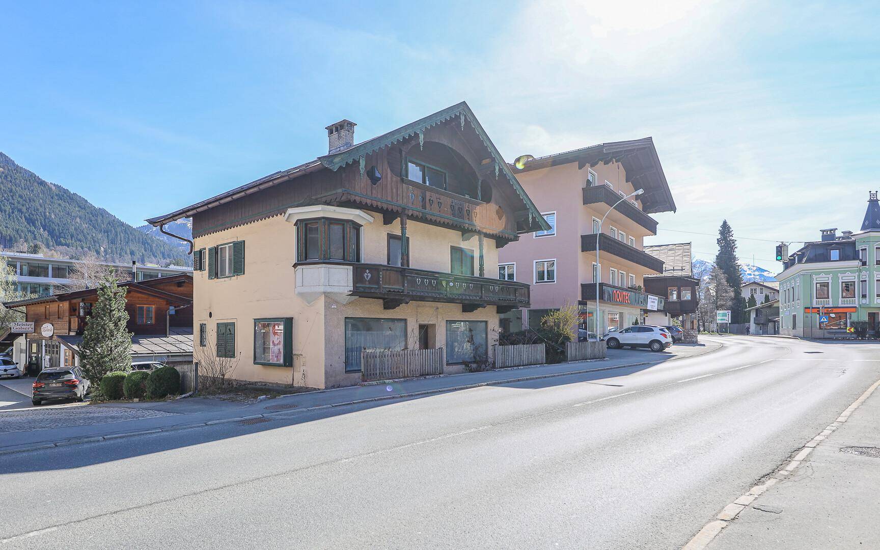 Das Anwesen an einer sonnigen Straße, umgeben von traditionellen Gebäuden und mit Bergblick.
