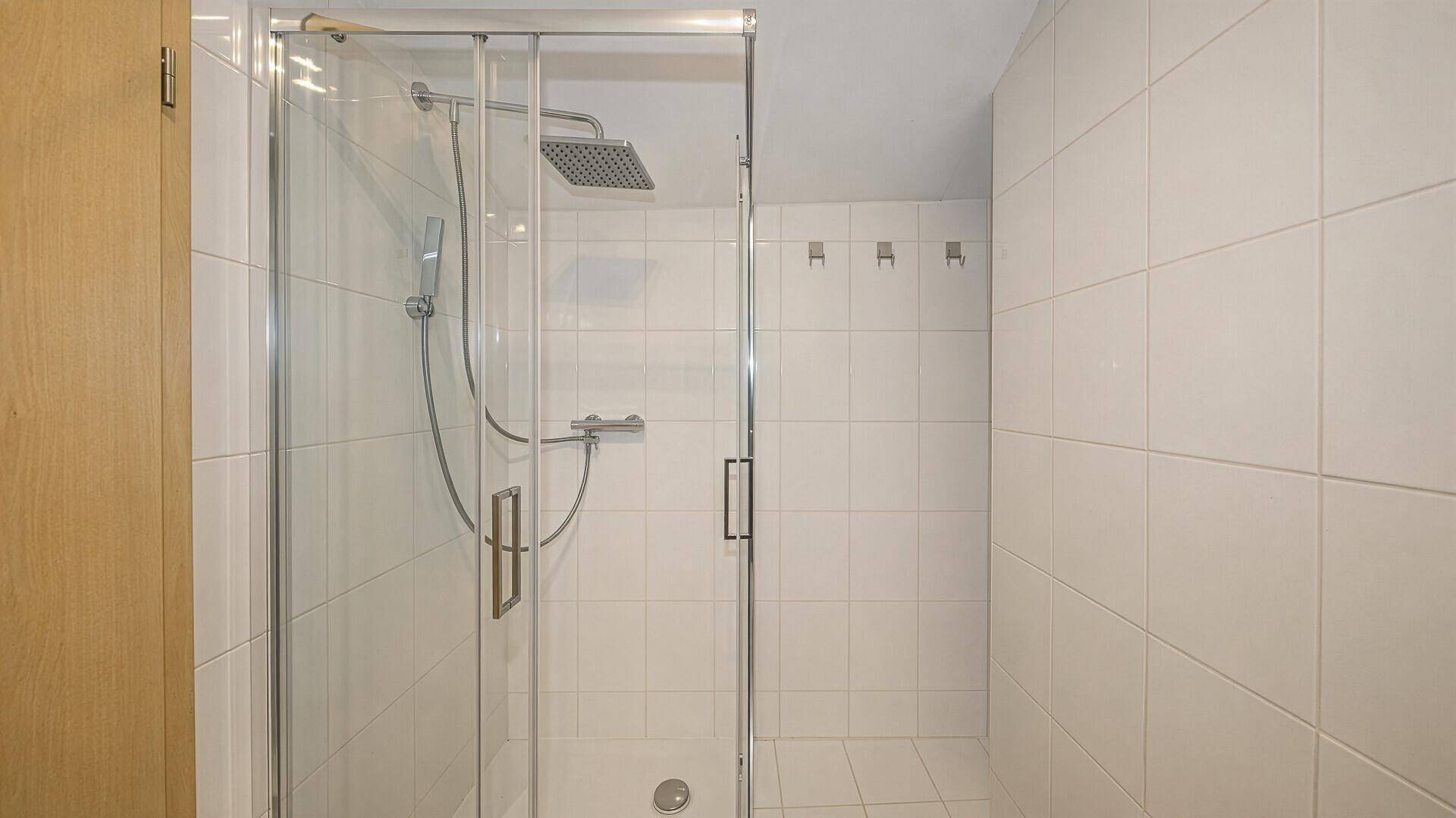 Modernes Badezimmer mit weiß gefliesten Wänden und einer geräumigen begehbaren Dusche.
