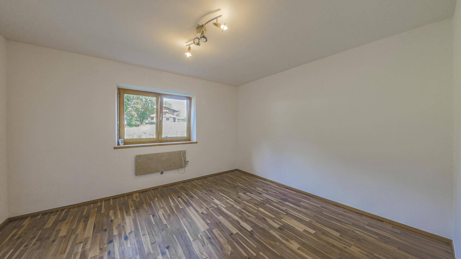 Leerer Raum mit Holzboden und Fenster, das viel Tageslicht hereinlässt.