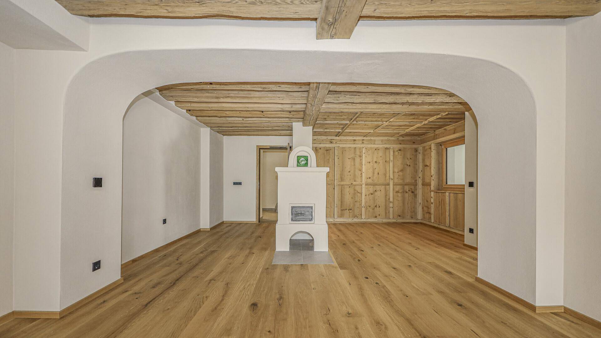 Rustikaler Wohnbereich mit Holzbalkendecke, Parkettboden und traditionellem Kachelofen.