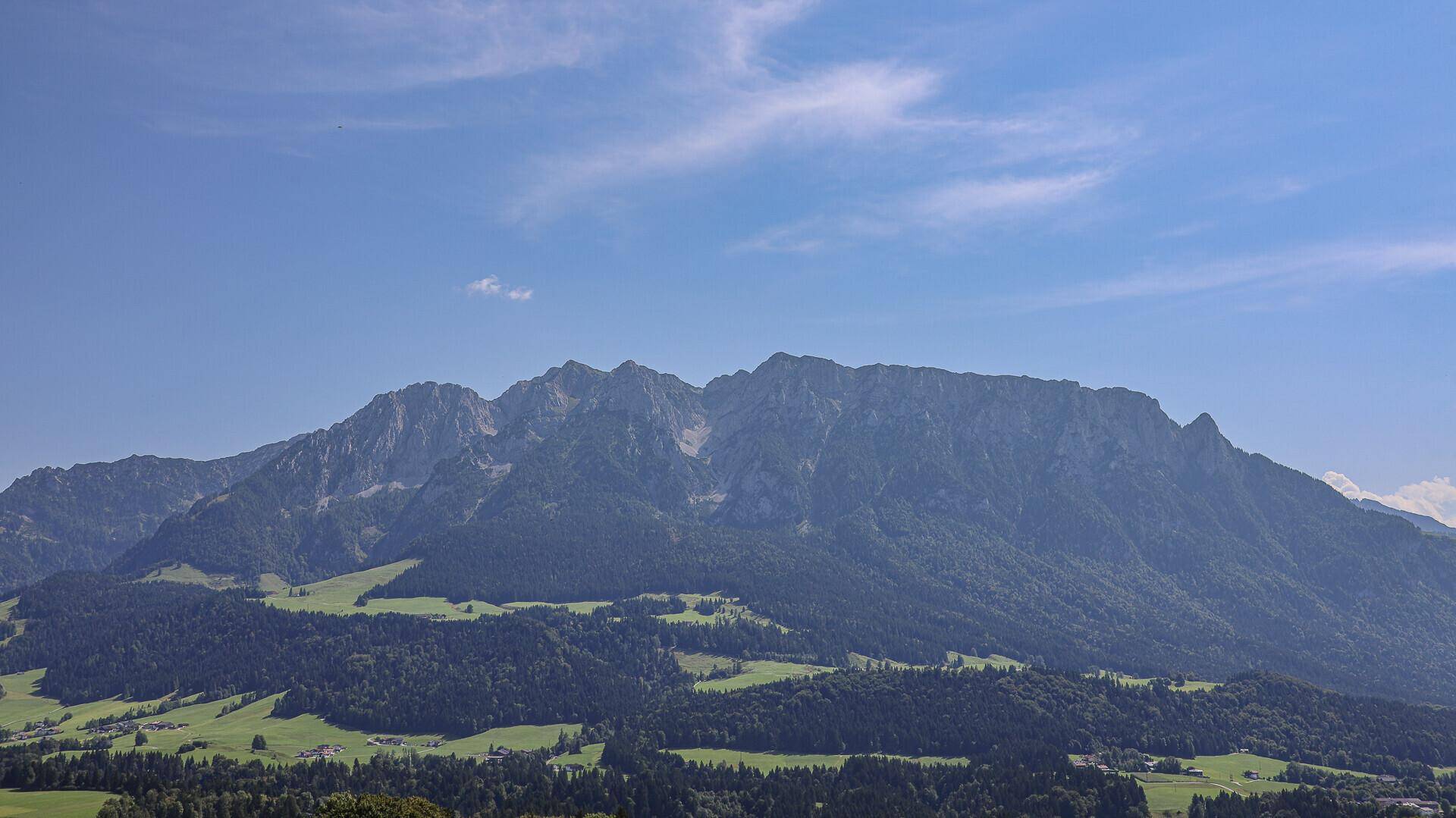 Beeindruckende Berglandschaft mit grünen Vorbergen und einem weiten, klaren blauen Himmel.