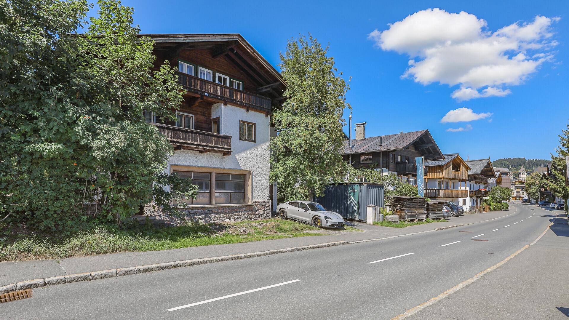 Traditionelles Haus mit Holzbalkonen und weißer Fassade, umgeben von Bäumen an einer Straße.