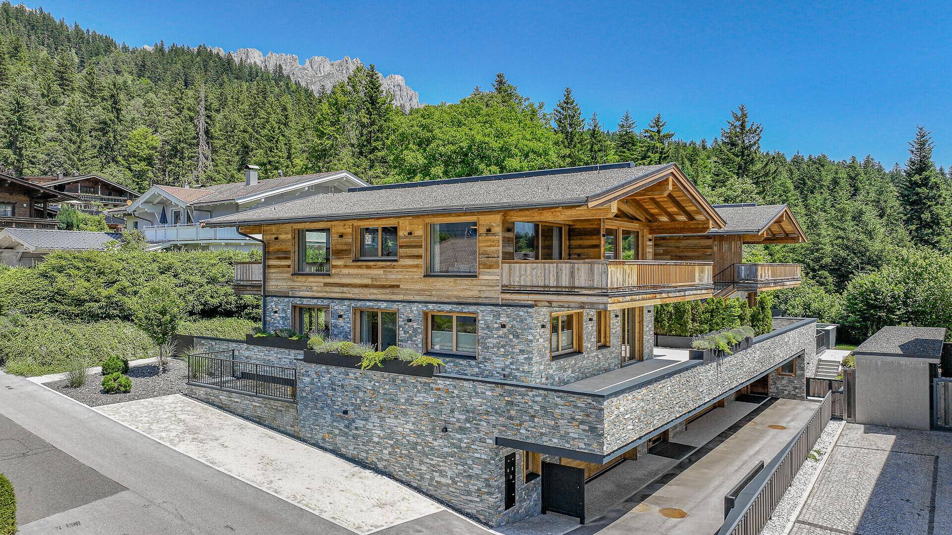 Neubau-Chalet mit moderner Holz- und Steinfassade, umgeben von alpiner Landschaft und viel Grün.