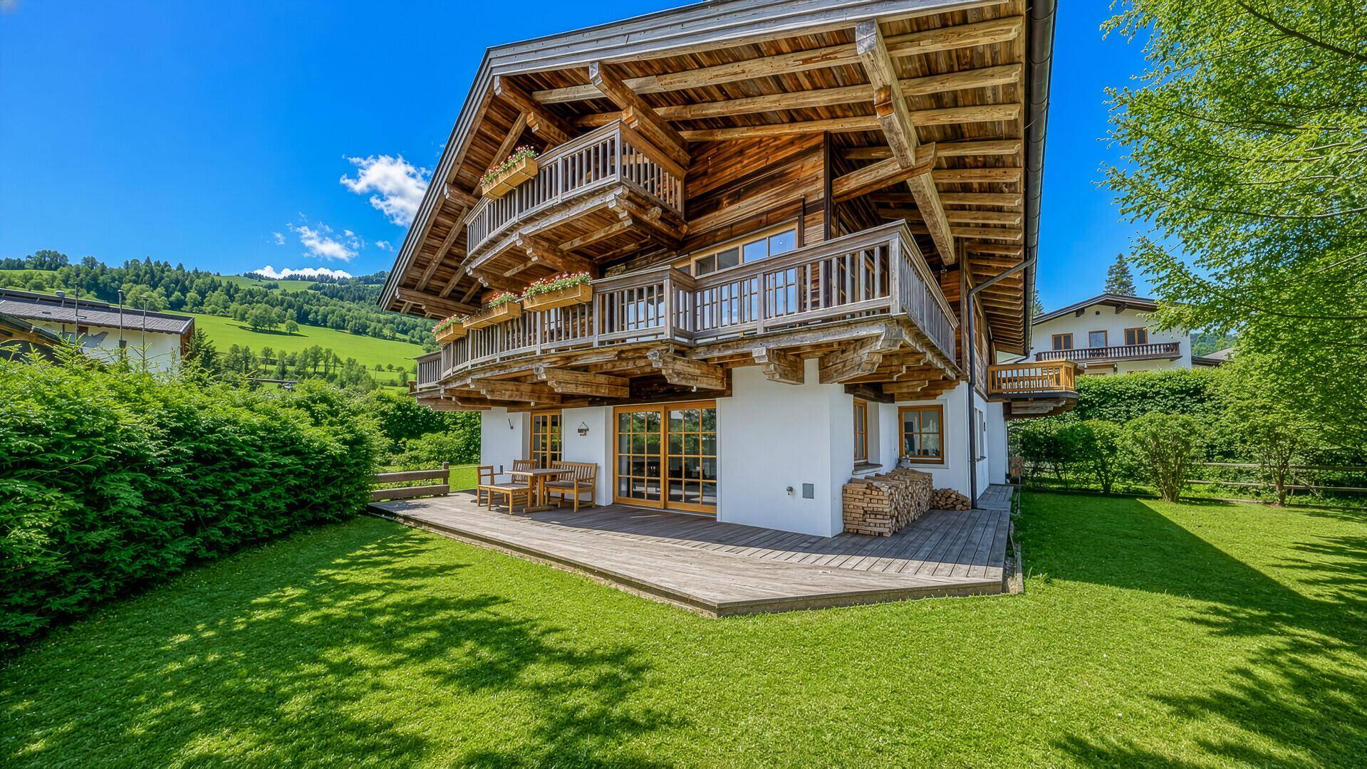 Großer Garten mit Rasenfläche und Holzterrasse, umgeben von grüner Natur.