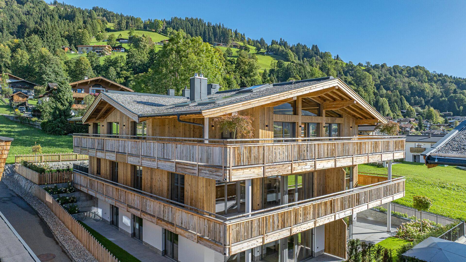 Attraktives Chalet-Gebäude mit Holzverkleidung und großen Fensterfronten in sonniger Lage.
