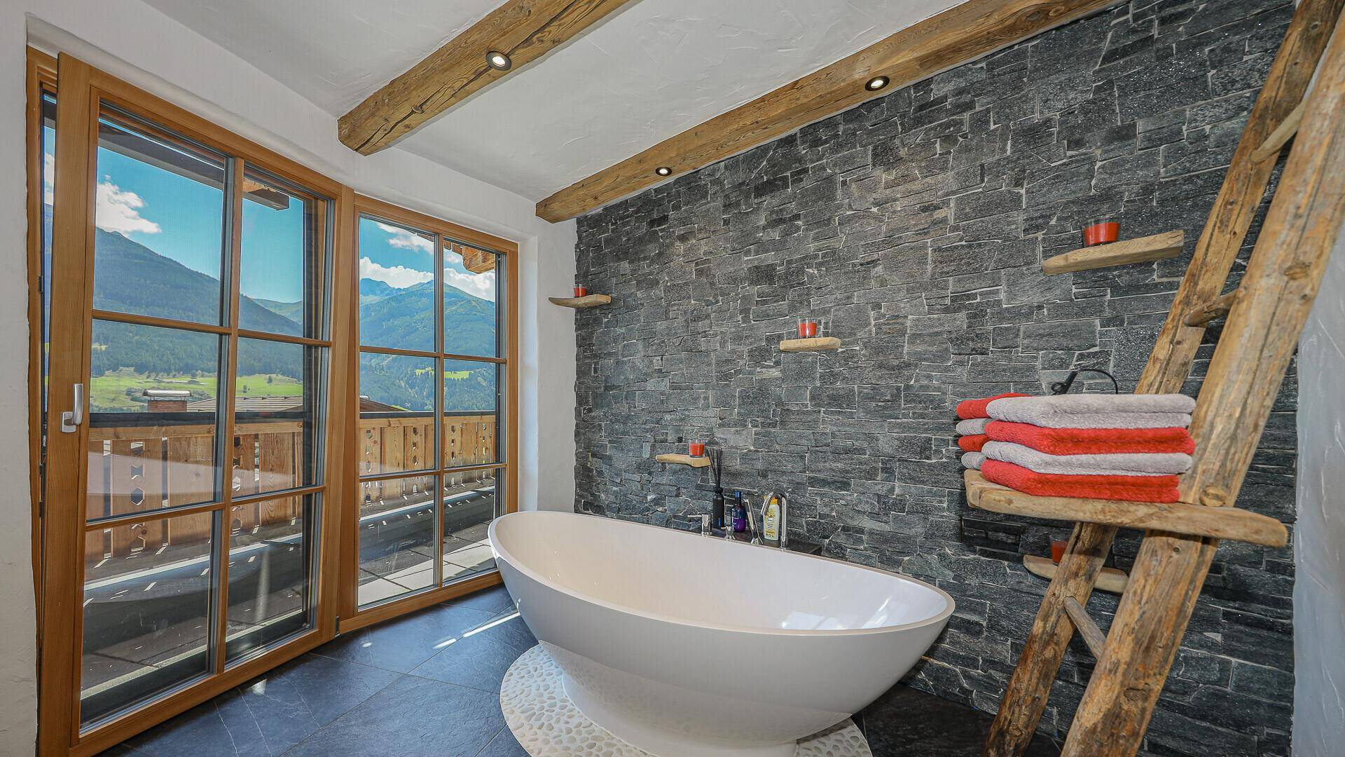 Modernes Badezimmer mit freistehender Badewanne, Steinwand und Bergblick durch große Fenster.