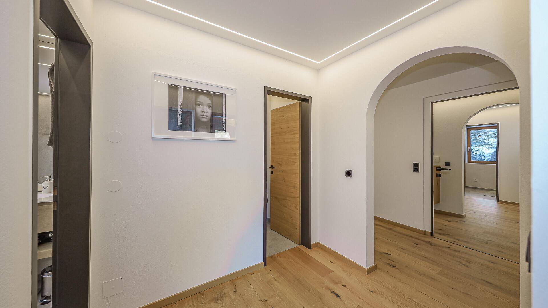 Heller Flur mit Holzboden, modernen Lichtleisten und eleganten Torbögen zu den Zimmern.