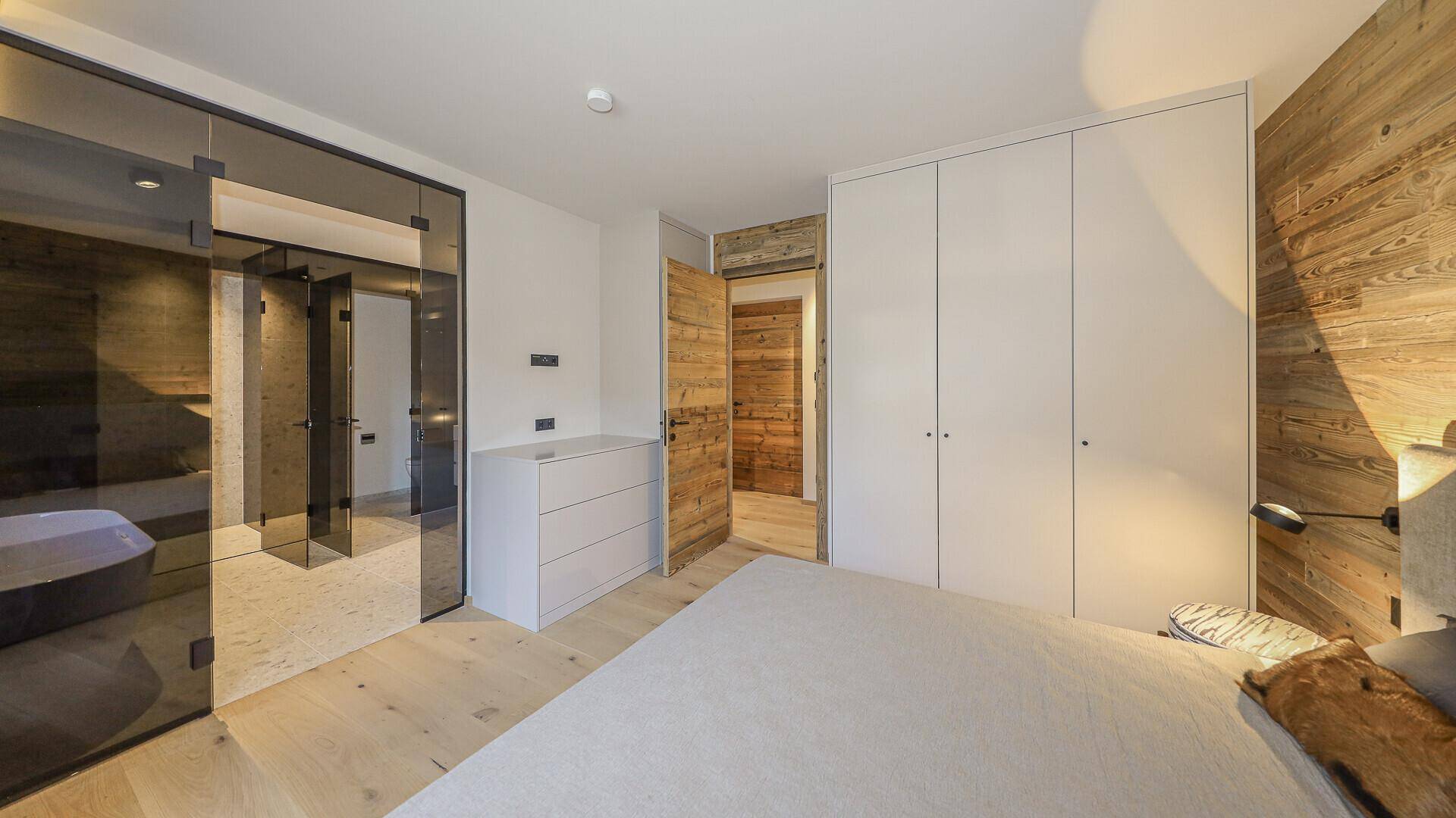 Modernes Schlafzimmer mit Holzwand, Einbauschränken und Glaszugang zum Bad.