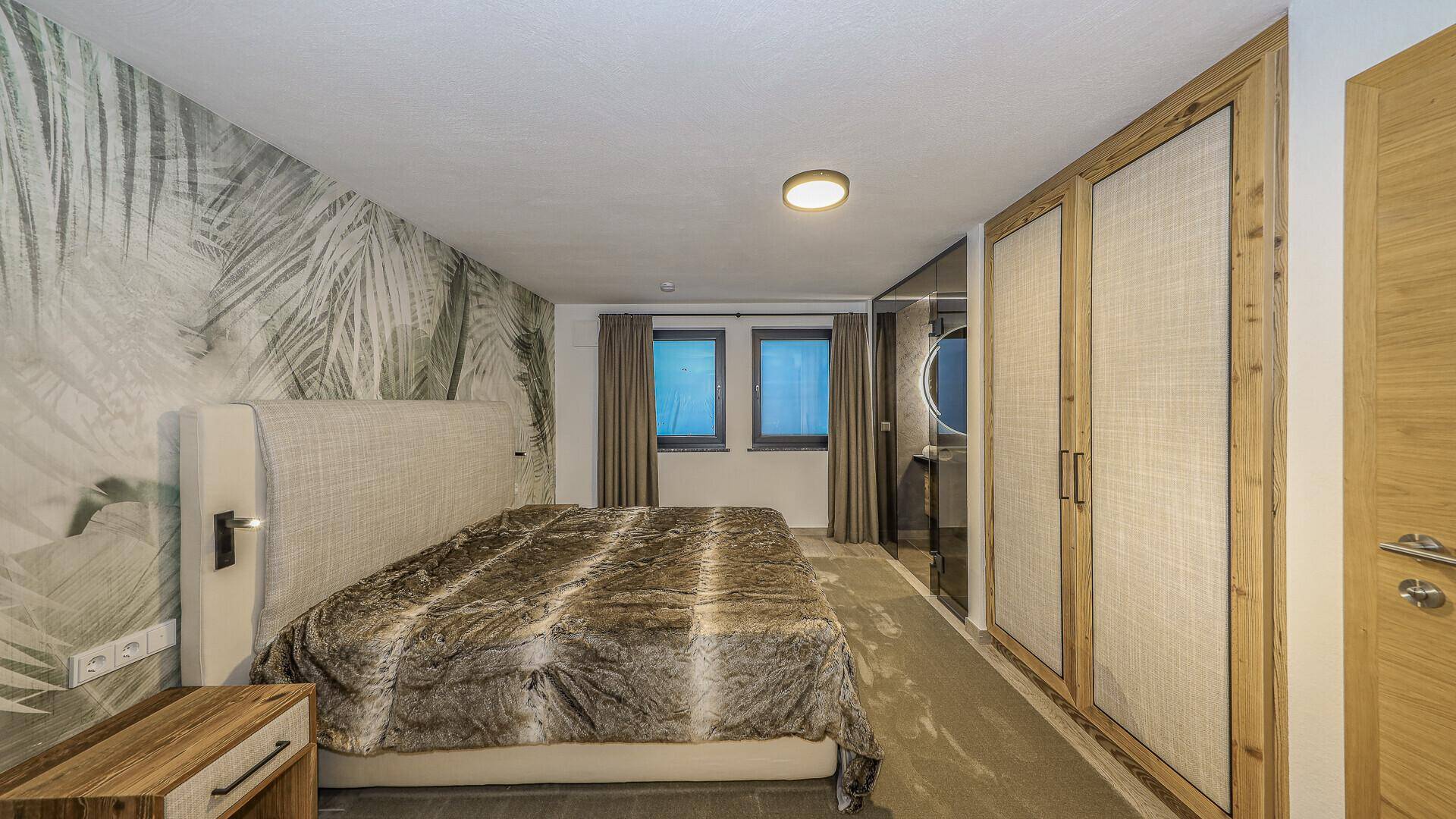 Schlafzimmer mit gemusterter Tapete, Einbauschränken und Zugang zum Badezimmer.