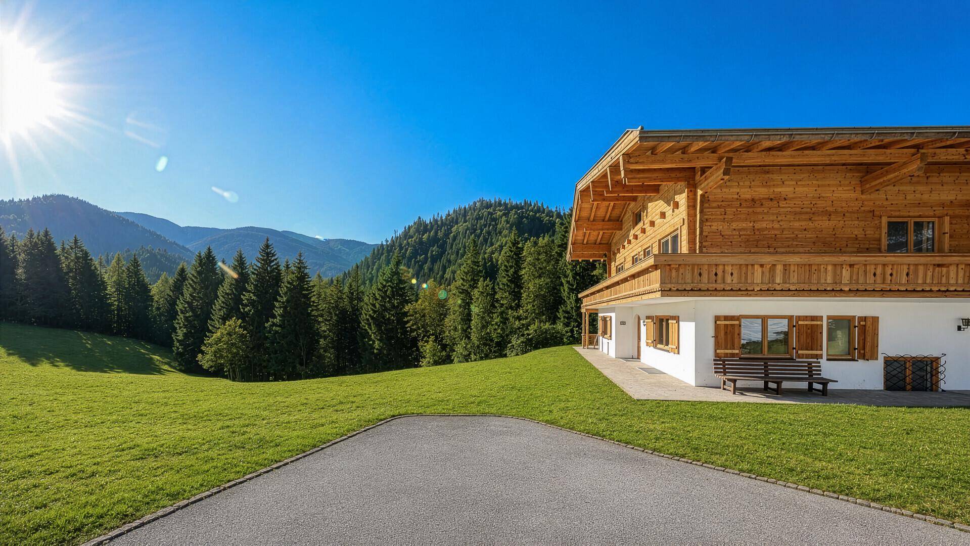 Sonnige Ansicht des Holzchalets mit gepflastertem Bereich und weitem Blick auf die Berge.