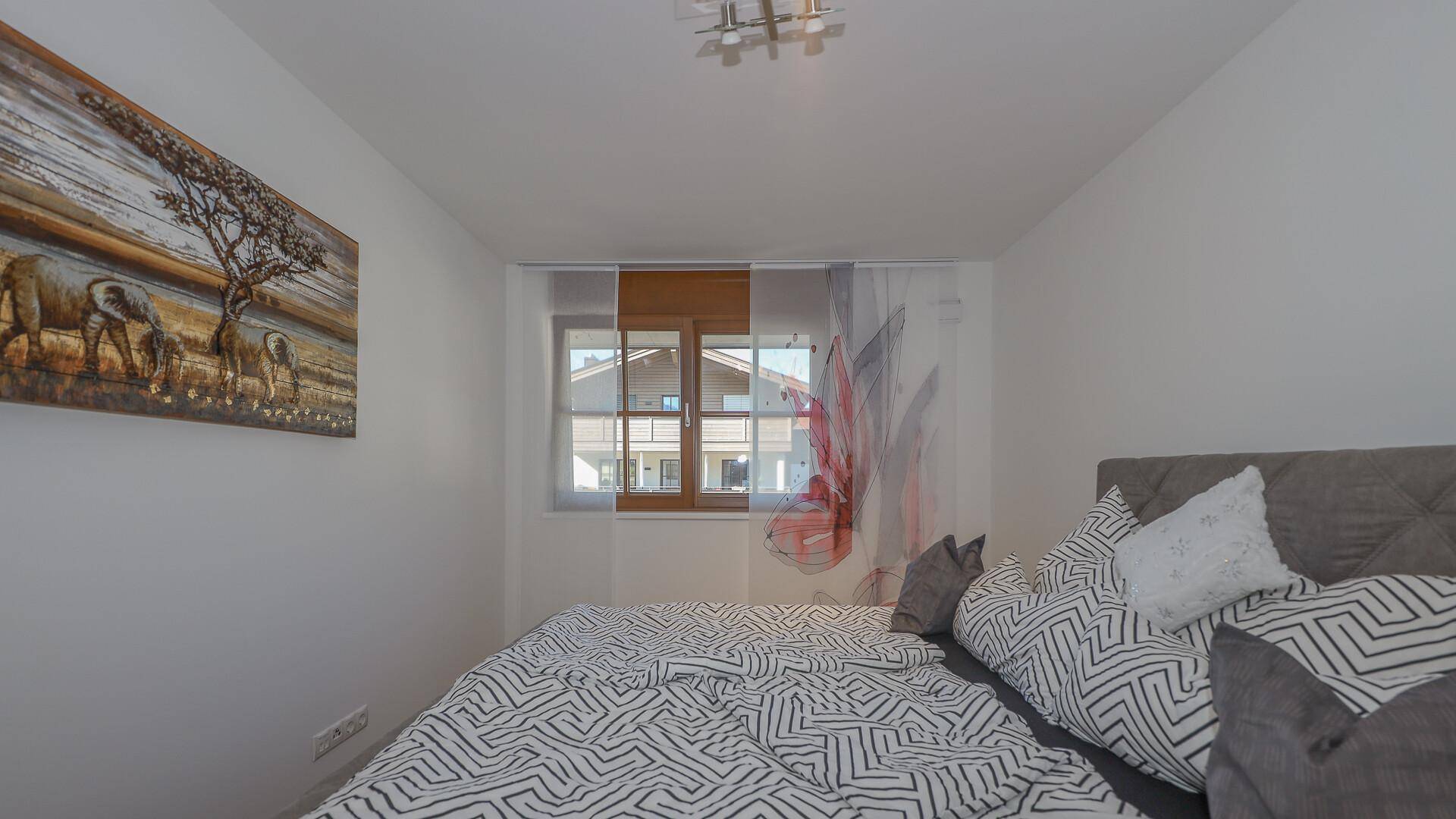 Schlafzimmer mit Doppelbett, Holzboden und Blick auf die umliegenden Häuser.