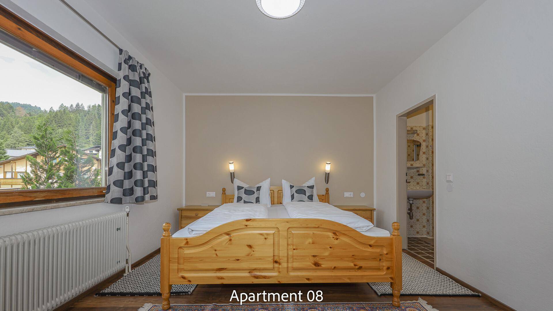 Helles Schlafzimmer von Apartment 08 mit Holzdoppelbett und Zugang zum Badezimmer.