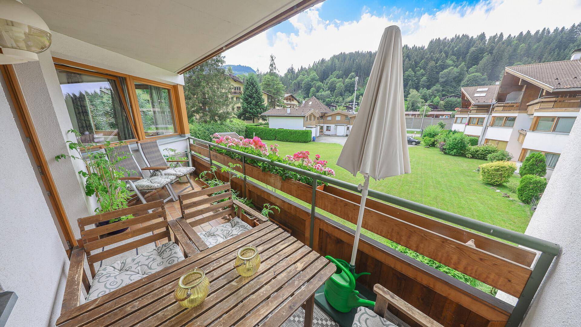 Möblierter Balkon mit Blumenkästen, Sonnenschirm und Blick auf den Garten und die Umgebung.