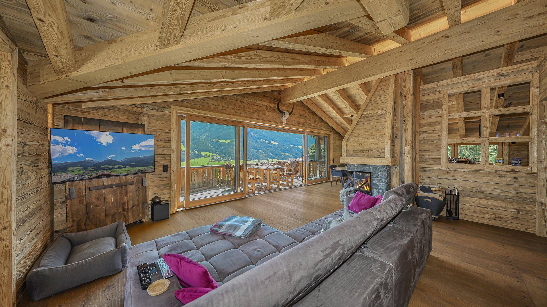 Gemütliches Wohnzimmer im Chalet-Stil mit Holzbalken, Kamin und Bergblick.