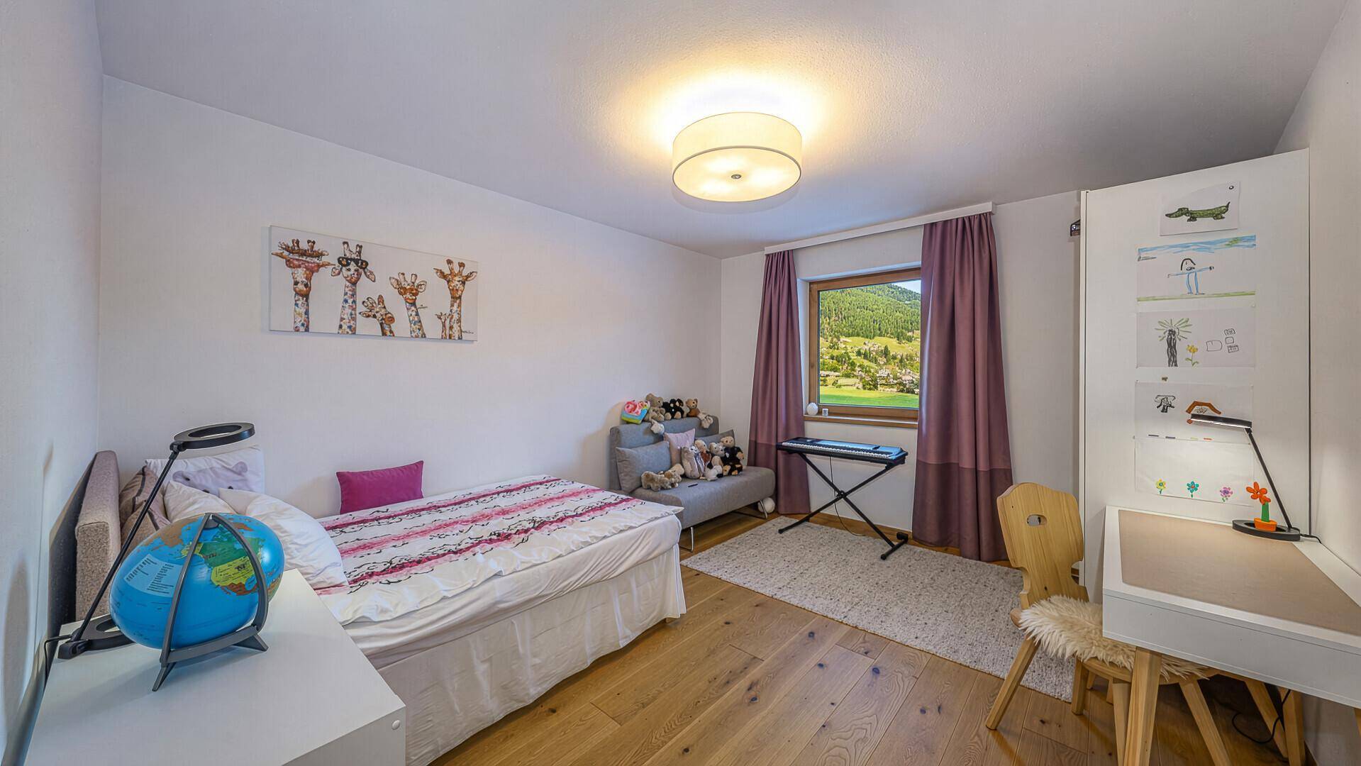 Kinderzimmer mit Bett, Schreibtisch, Kleiderschrank und Fenster mit Blick auf die Landschaft.