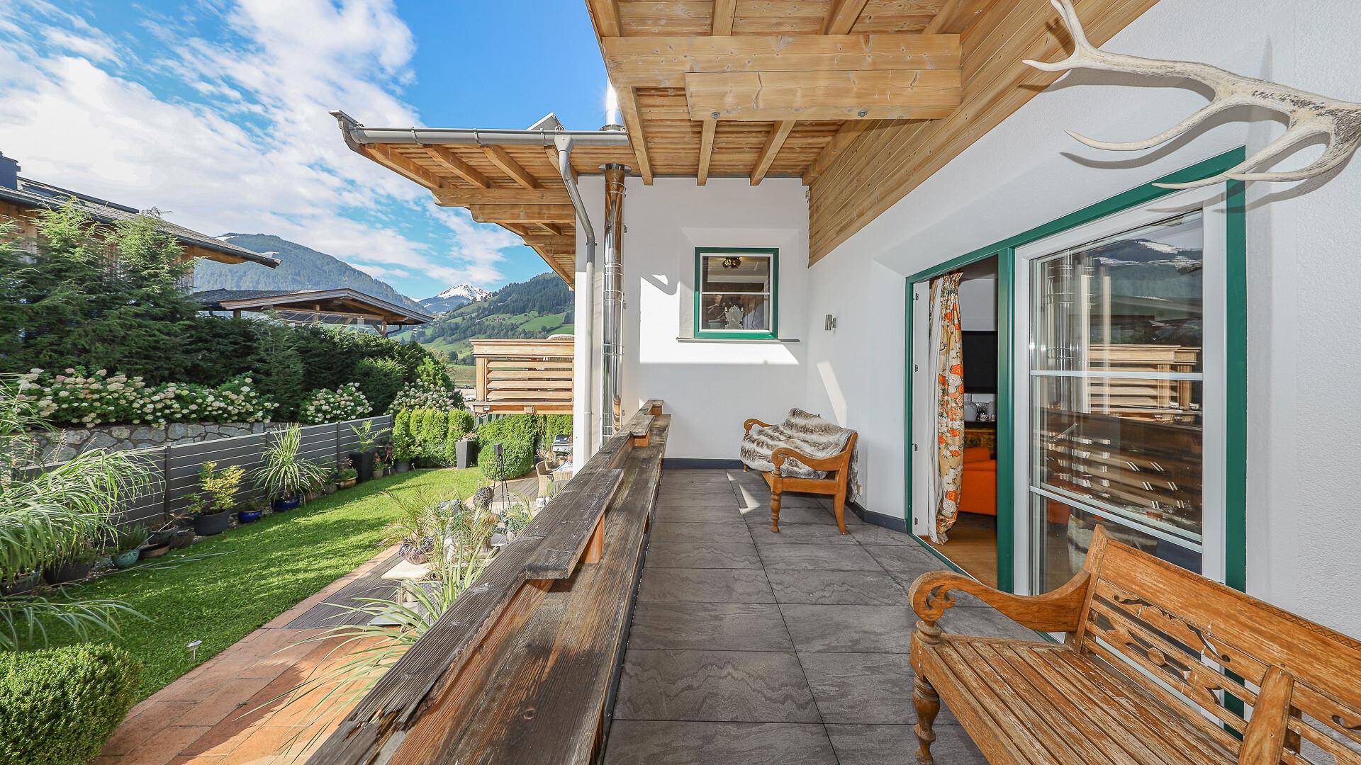 Geräumige Terrasse mit Holzbänken und Zugang zum gepflegten Garten, umgeben von Natur.