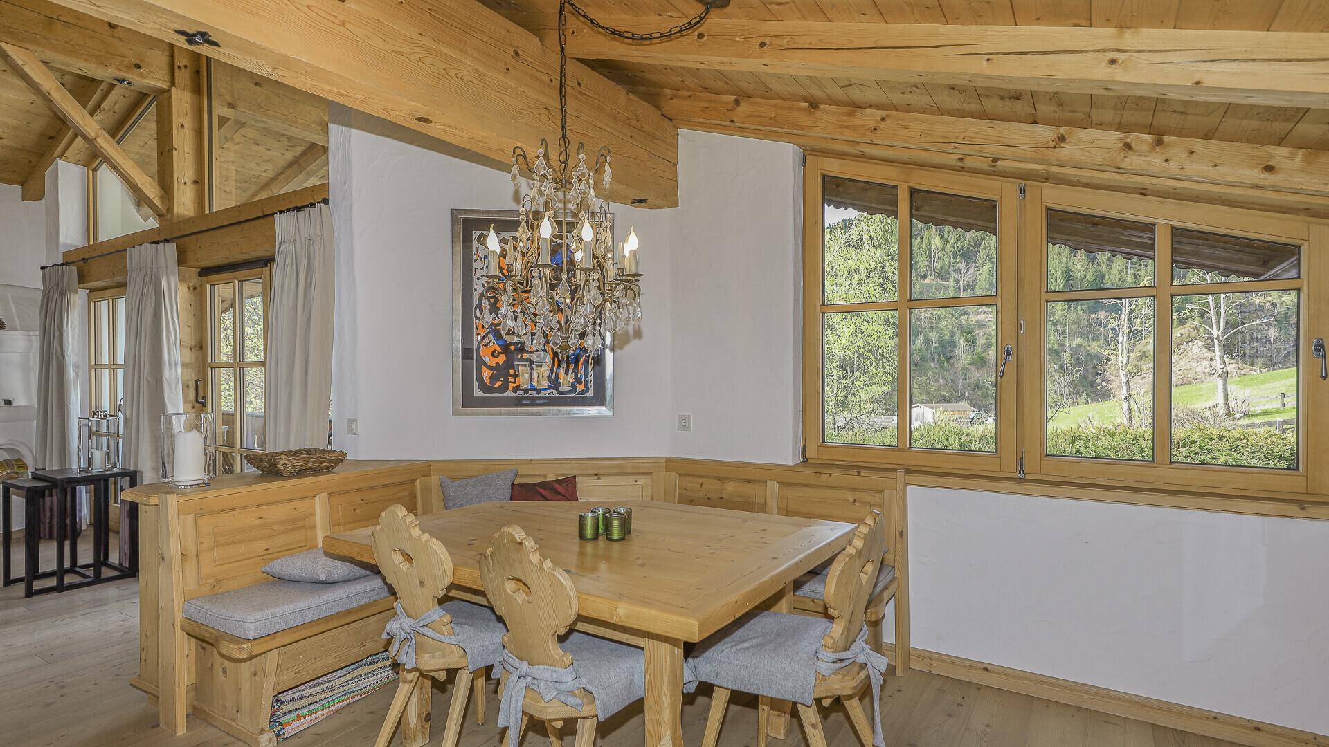 Gemütlicher Essbereich mit Holztisch und Eckbank, umgeben von Fenstern mit Bergblick.