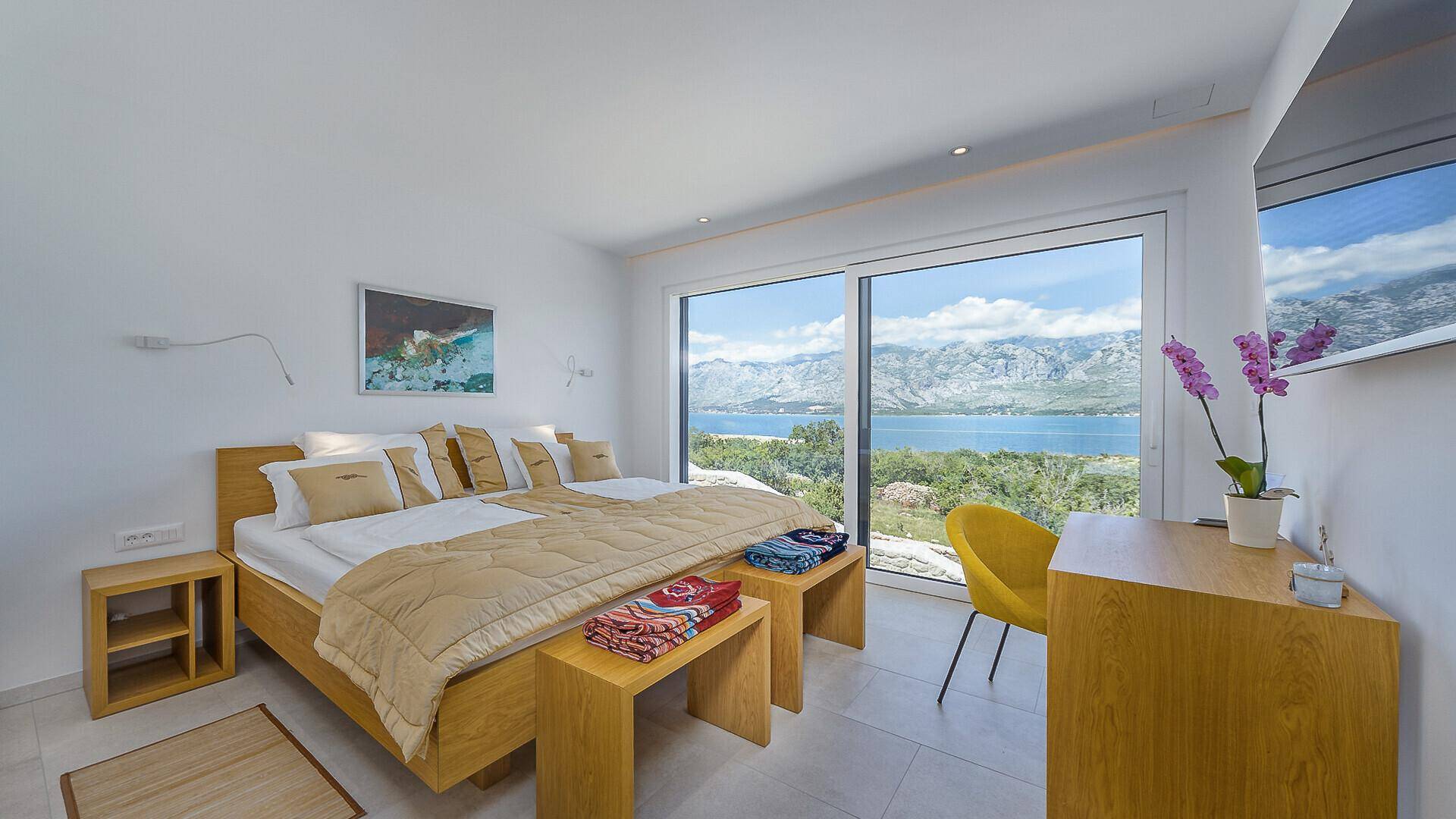 Gemütliches Schlafzimmer mit Holzbett, Schreibtisch und großen Fenstern, die einen herrlichen Meerblick bieten.