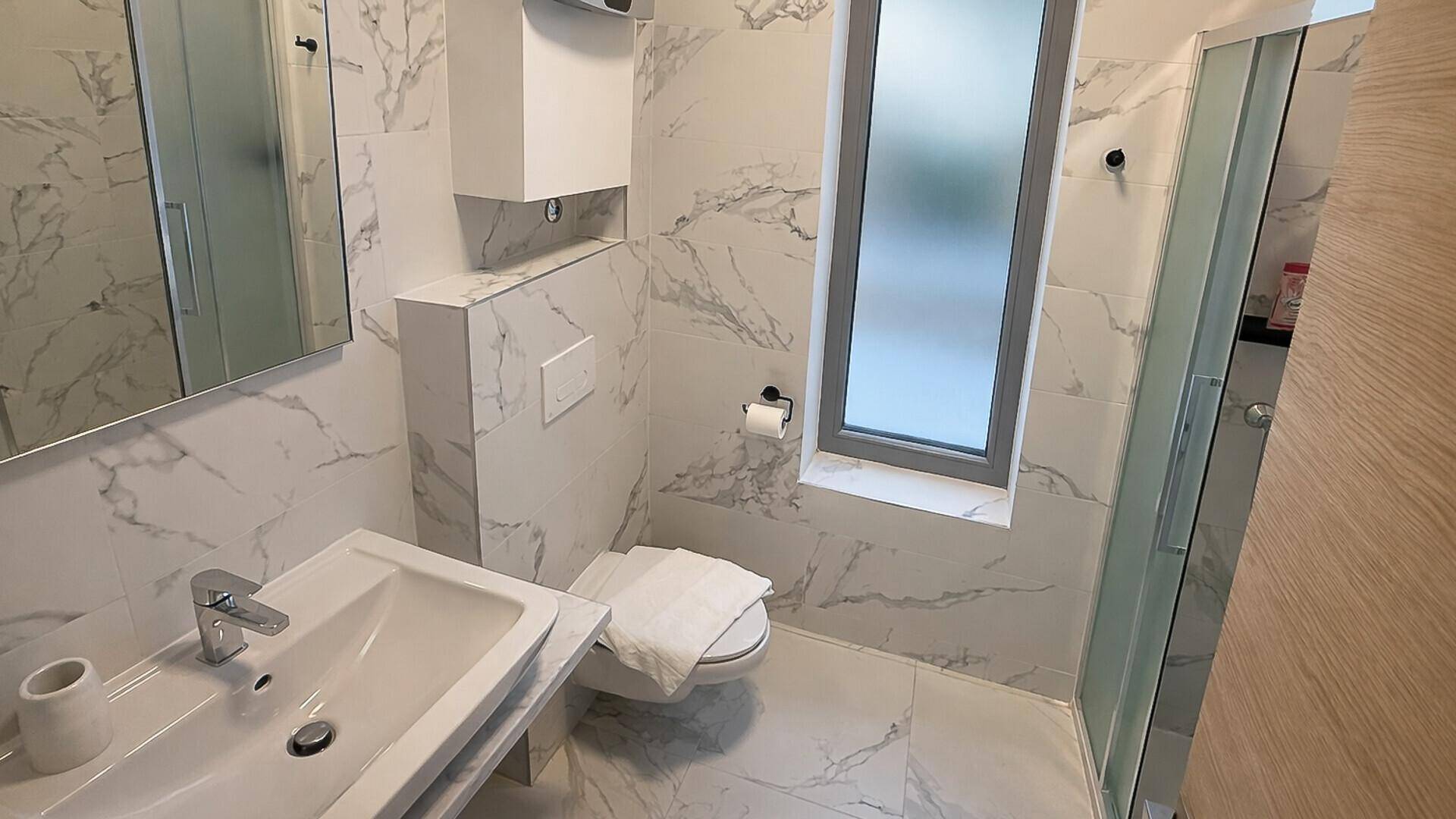 Modernes Badezimmer mit Marmorfliesen, wandhängendem WC und Duschkabine.
