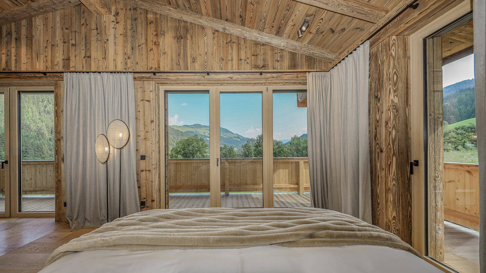 Schlafzimmer mit Holzwänden, großem Bett und bodentiefen Fenstern mit Zugang zum Balkon.