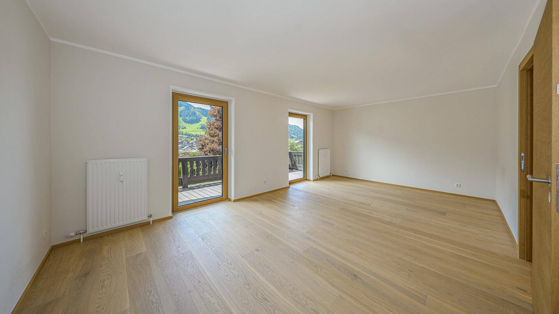 Heller, unmöblierter Raum mit Holzboden und zwei Zugängen zu Balkonen mit Bergblick.