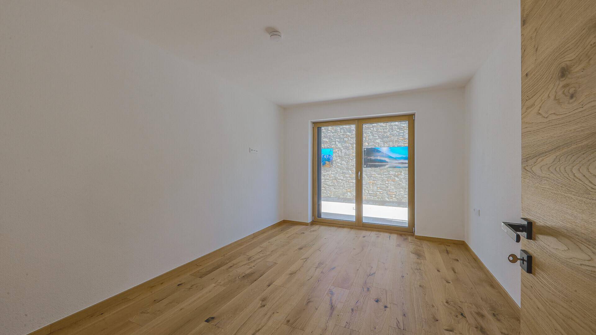 Heller Raum mit Holzboden und großen Schiebetüren, die viel Licht hereinlassen und Zugang nach draußen bieten.
