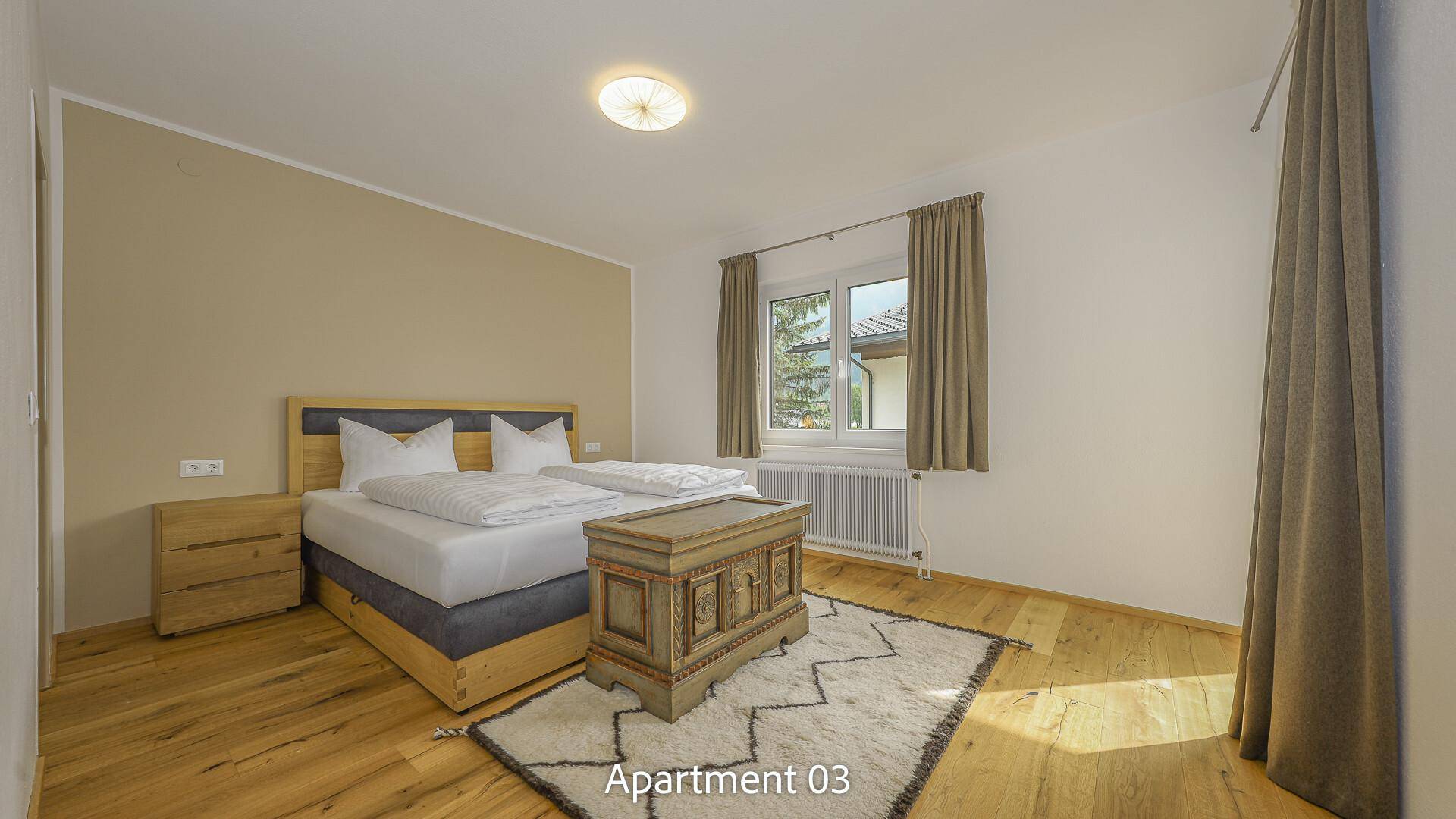 Schlafzimmer von Apartment 03 mit Doppelbett, Nachttischen und einer dekorativen Holztruhe auf Holzboden.