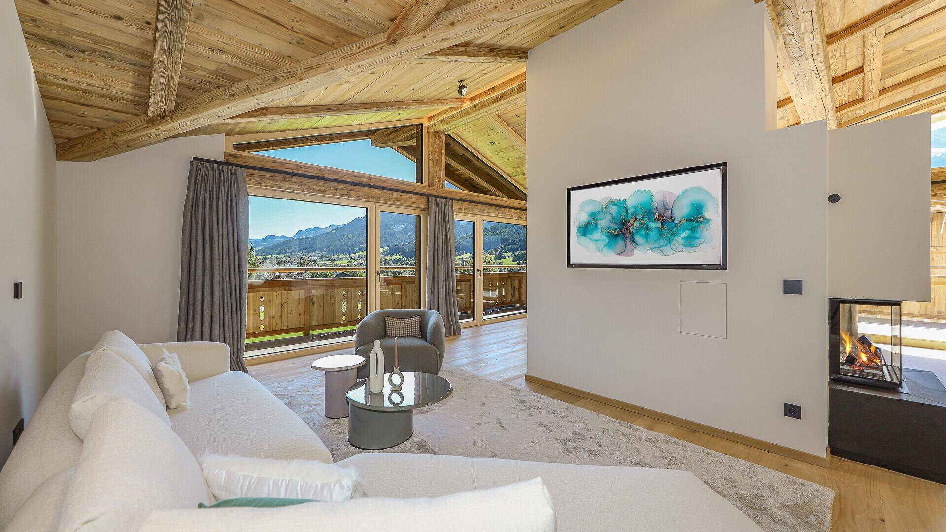 Heller Wohnbereich mit bequemen Möbeln, Kamin und großen Fenstern mit Panoramablick auf die Berge.